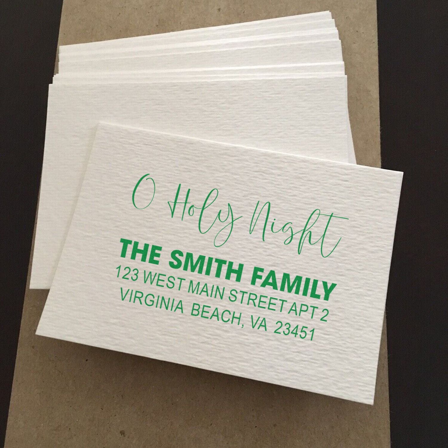 Custom rubber stamp for holiday napkins with O Holy Night, family name, and address in green on white cocktail napkins.