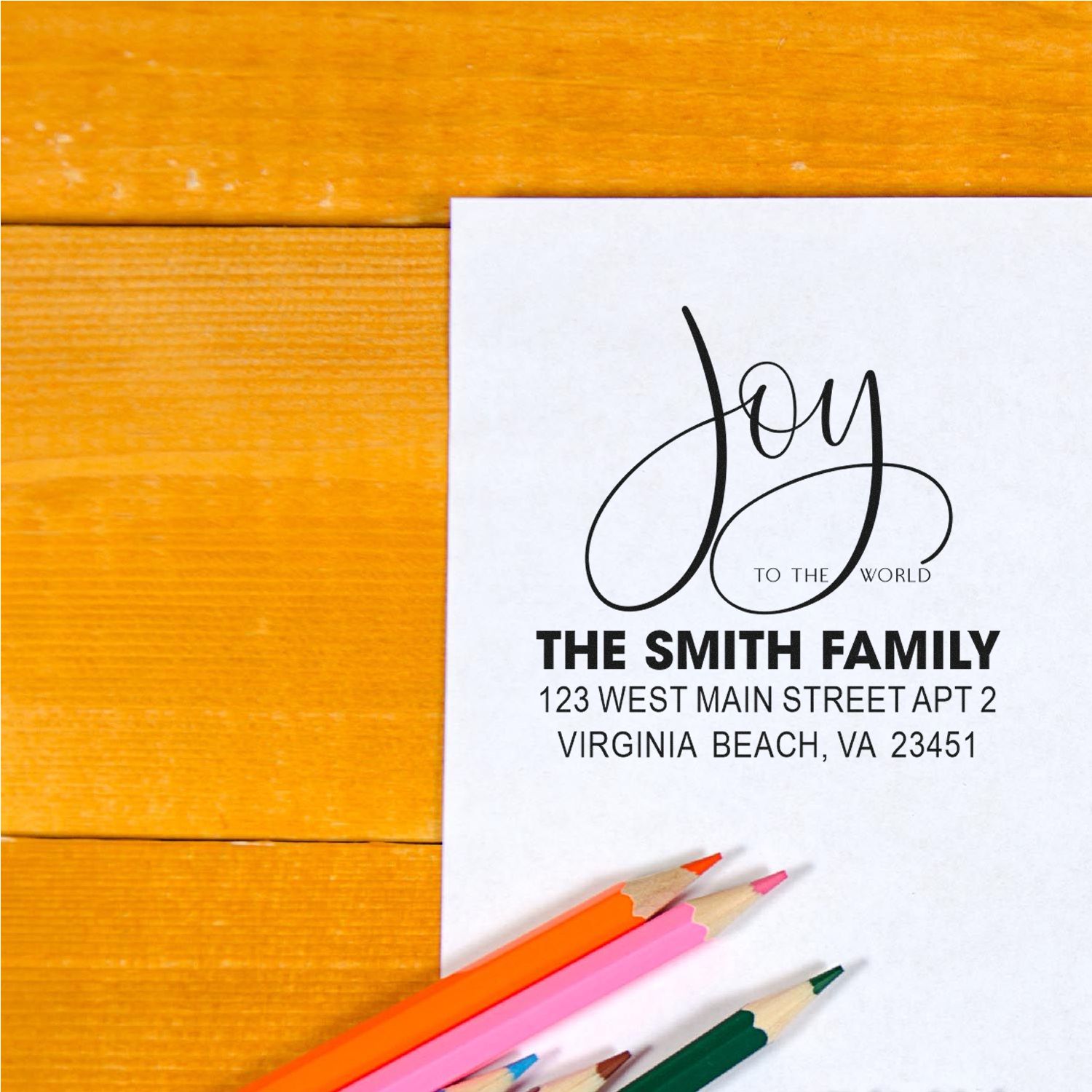 Custom family return address rubber stamp with Joy to the World design on stationery, shown with colored pencils