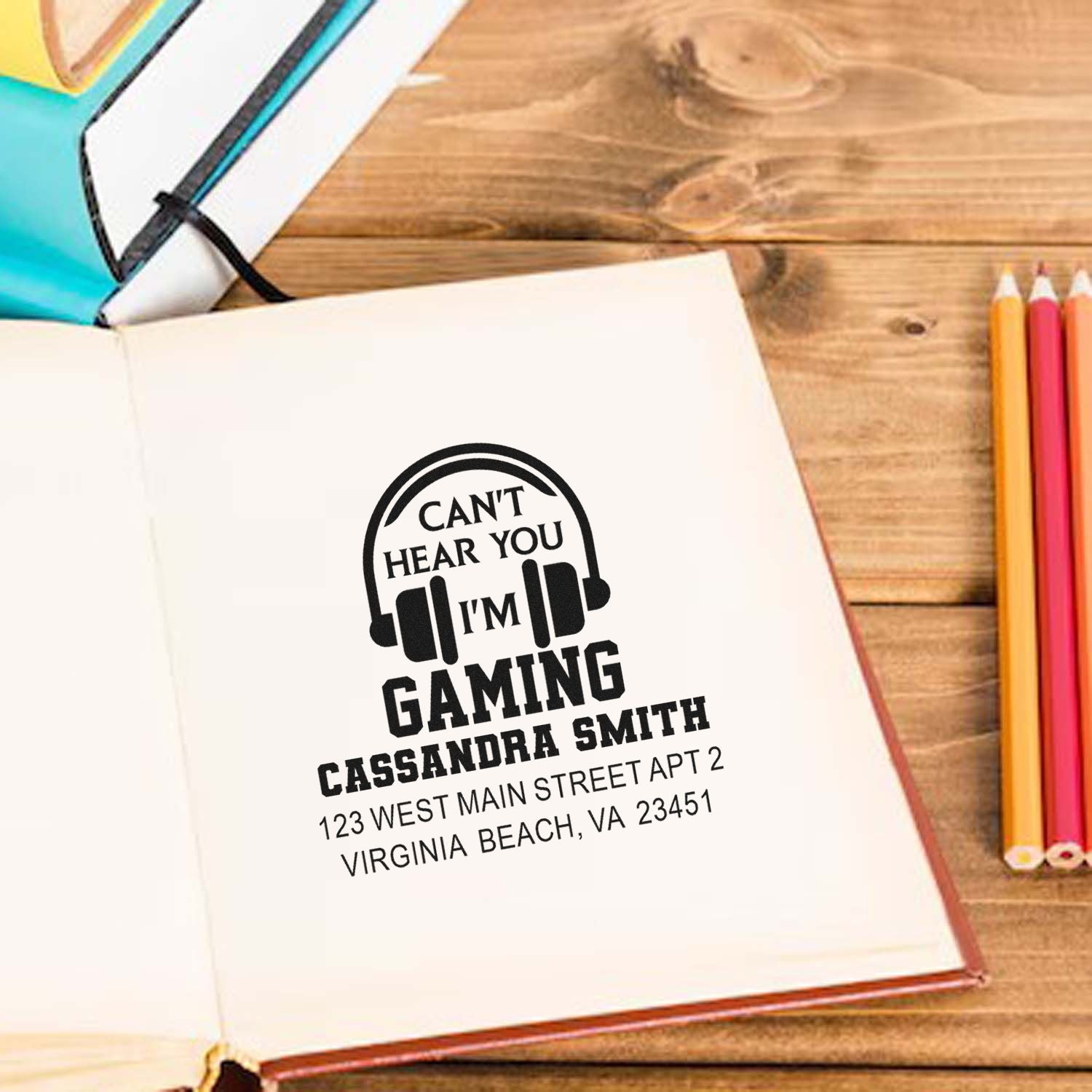 Custom gamer rubber stamp impression with headphones icon, personalized name, and address on a notebook.