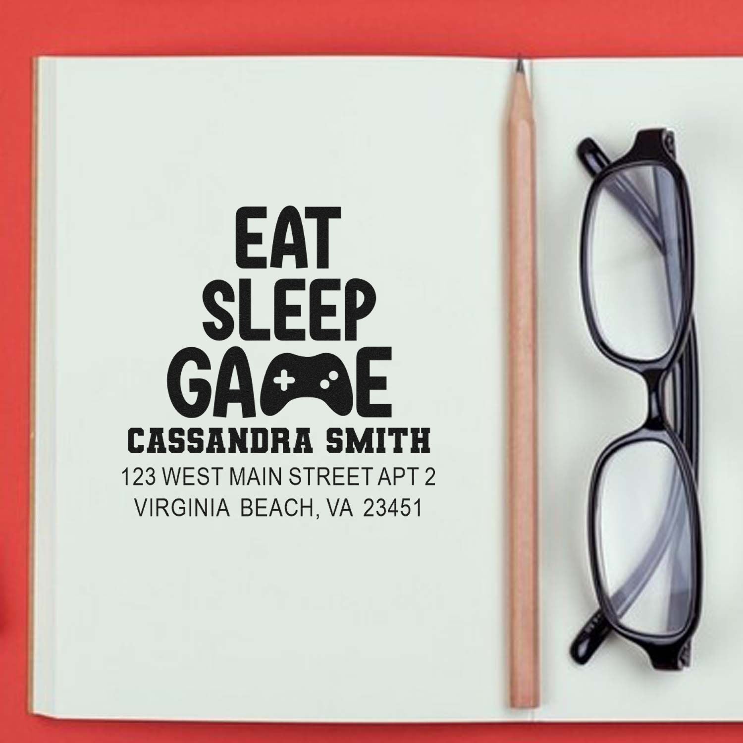 Personalized gamer return address rubber stamp with Eat Sleep Game design, name, and address on notebook.