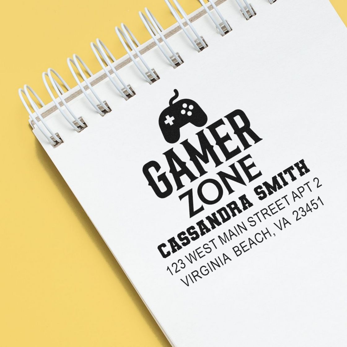 Custom gamer zone rubber stamp on notebook, featuring a gamer logo, name, and address for personalized branding.