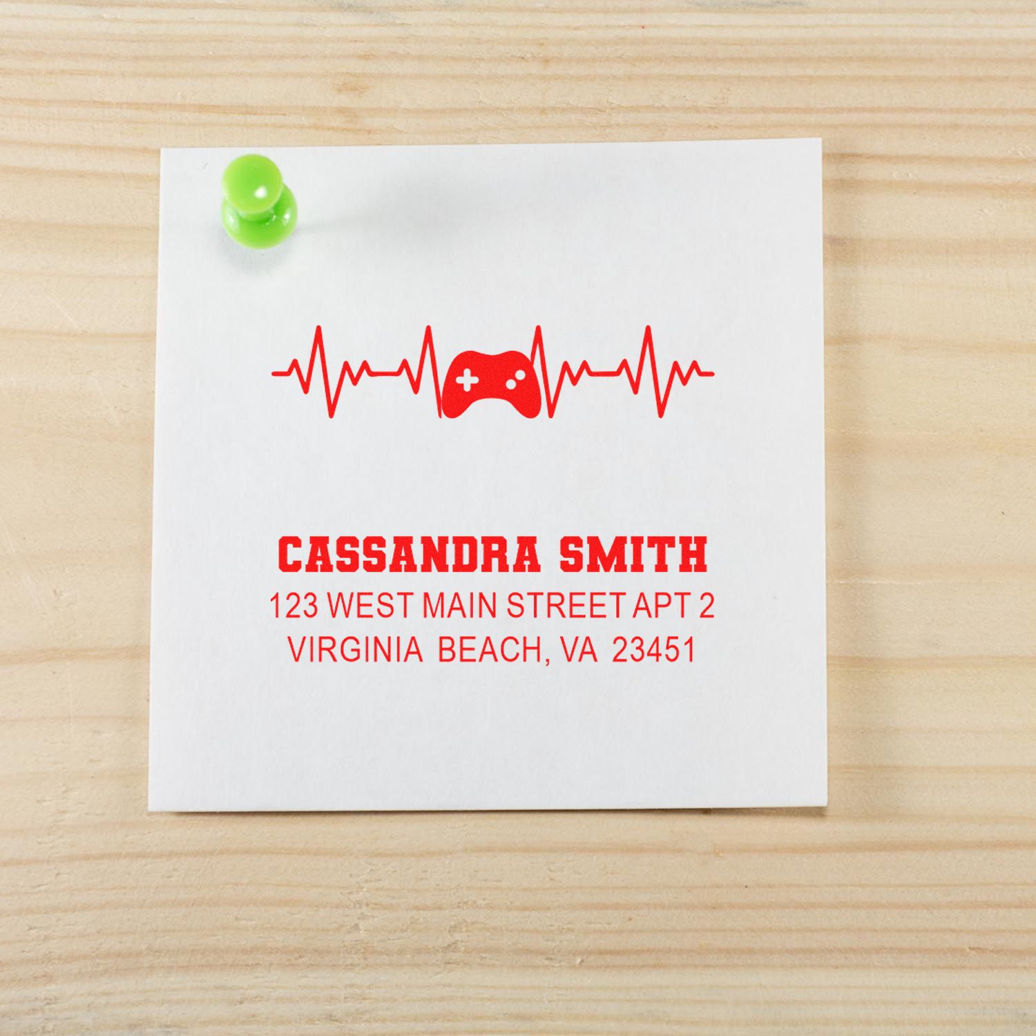 Custom rubber address stamp with gaming heartbeat design for Cassandra Smith, shown in red ink on paper.