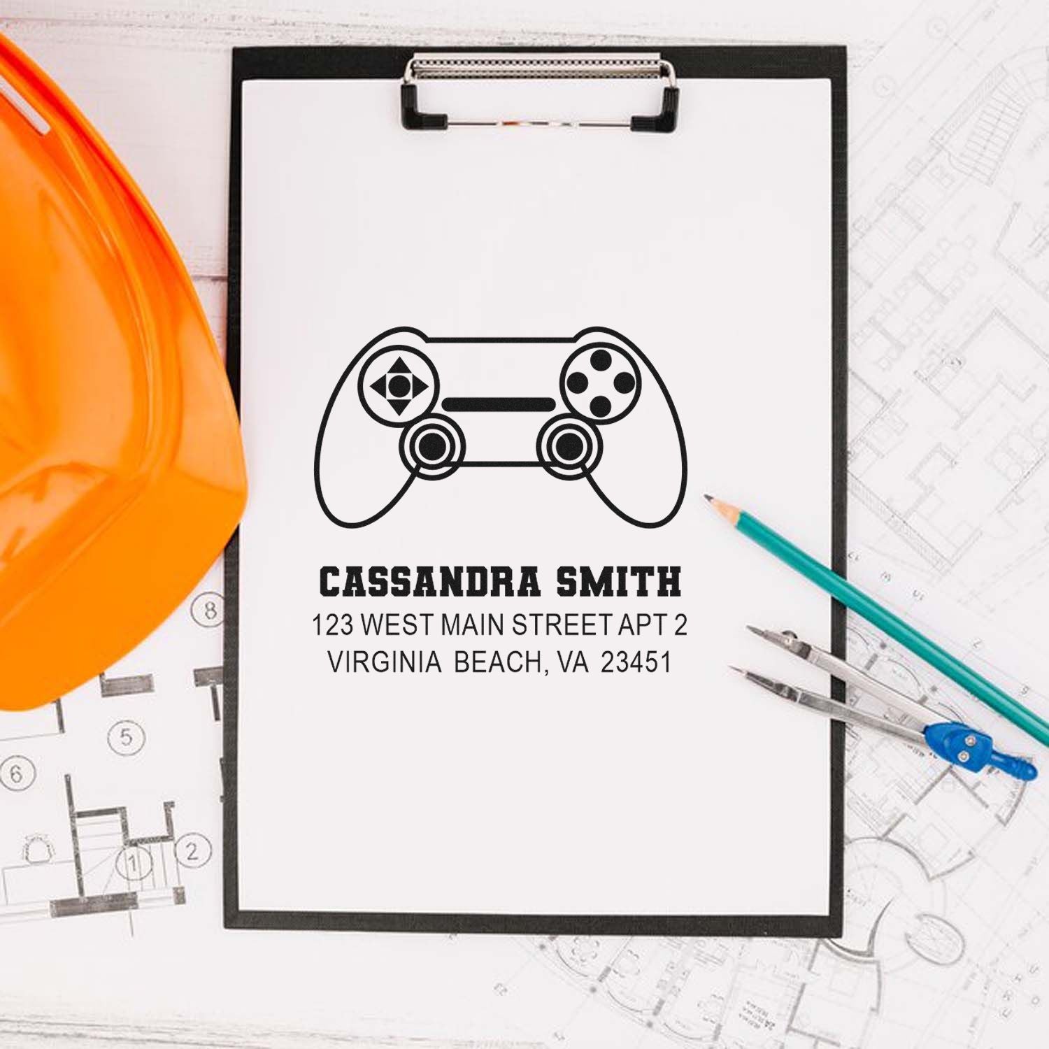 Custom rubber stamp with game controller design, name, and address for return mailing on a clipboard.