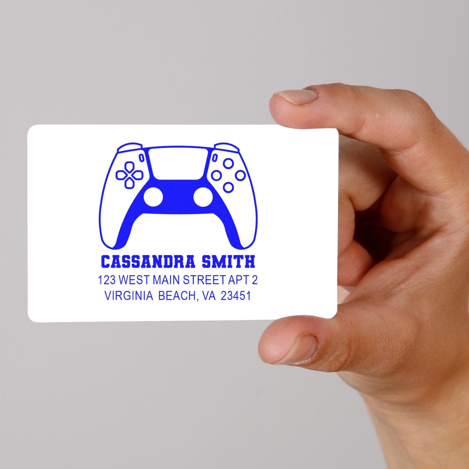 Hand holding custom rubber stamp design with game controller logo, name, and address for personalized mailing.