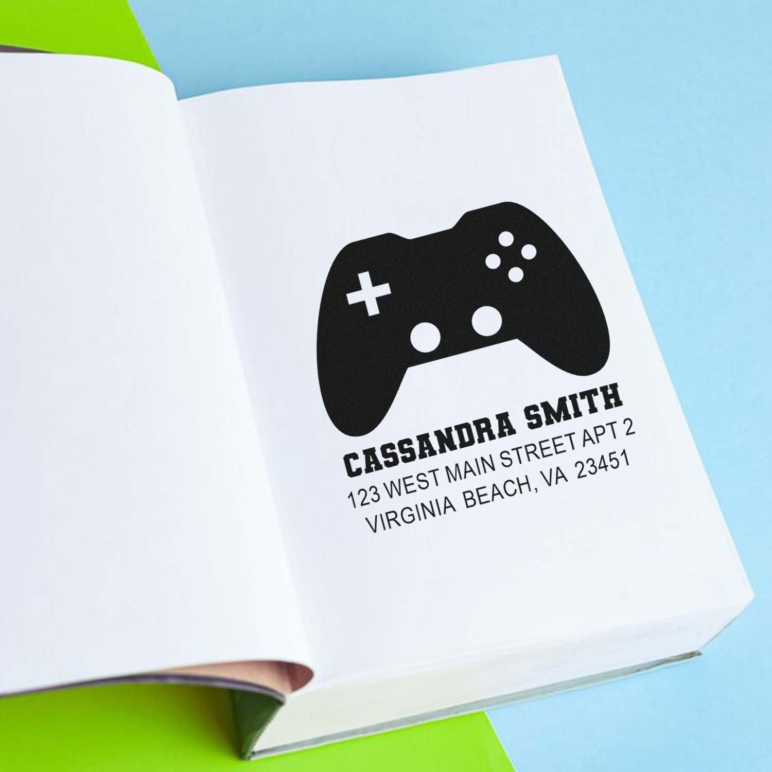 Custom gamer address rubber stamp on notebook page with controller icon, name, and Virginia Beach address.