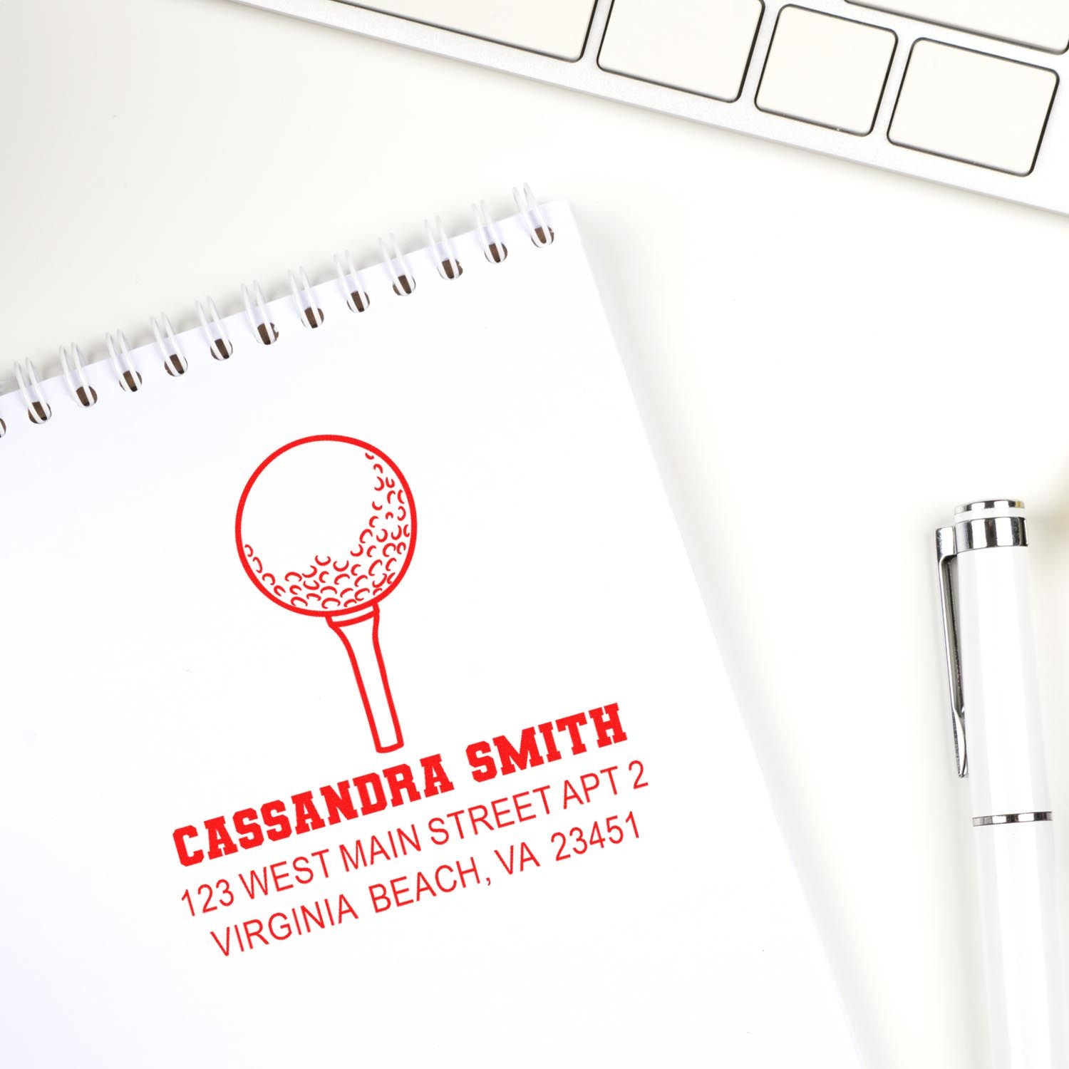Personalized golf address rubber stamp with name and mailing address stamped on a notebook beside a pen and keyboard.