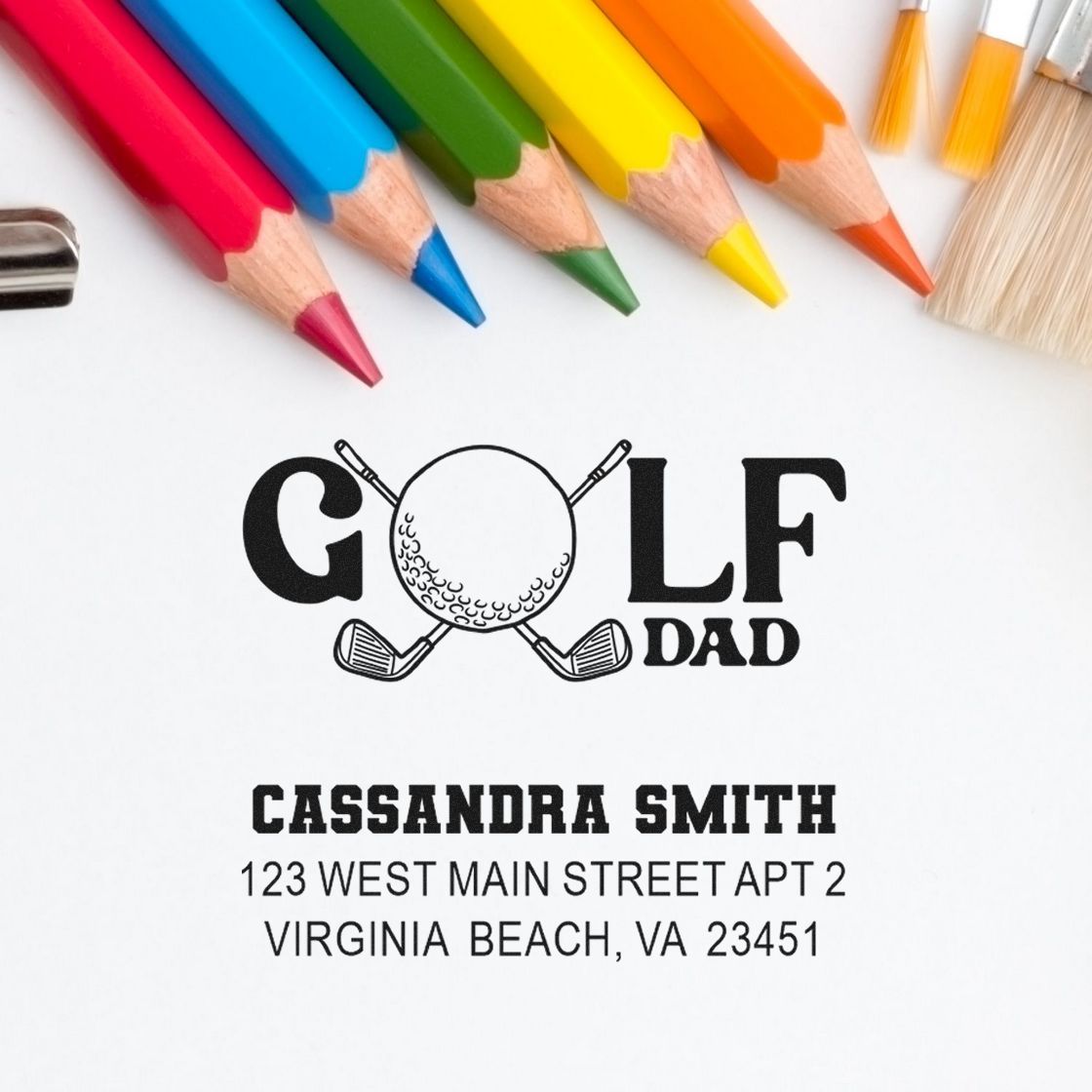 Custom golf dad address stamp design with personalized name and address, shown with colored pencils.