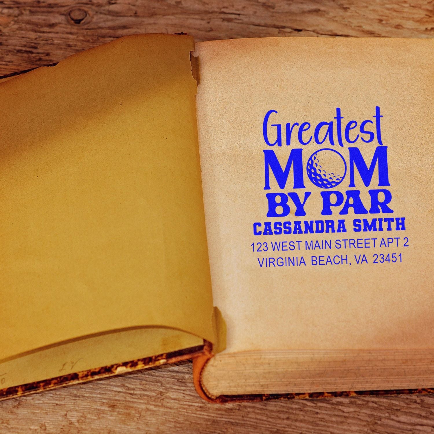 Custom rubber stamp on open book pages featuring a blue Greatest Mom by Par personalized name and address design.