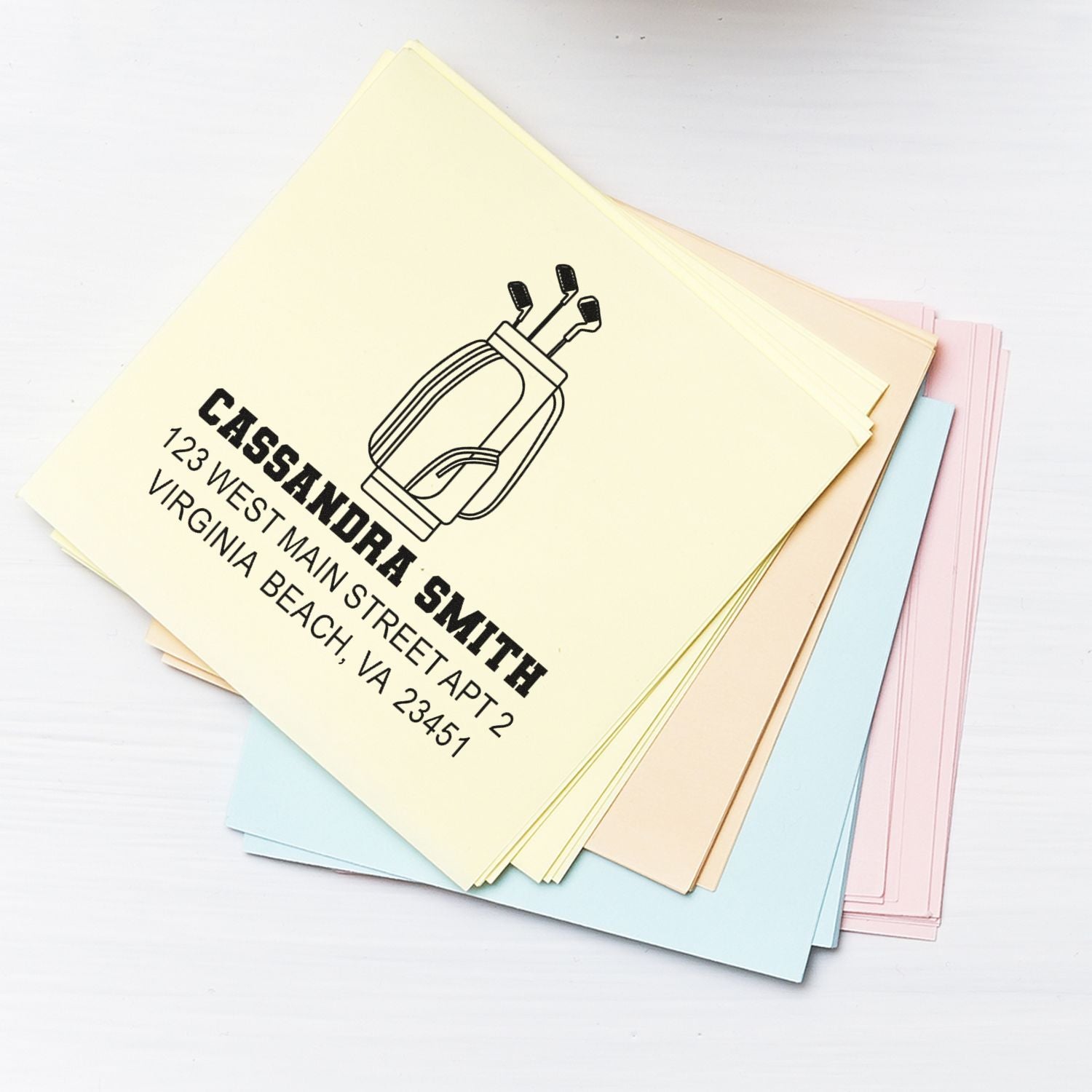 Custom return address rubber stamp for Cassandra Smith with golf club logo, shown on pastel paper samples.