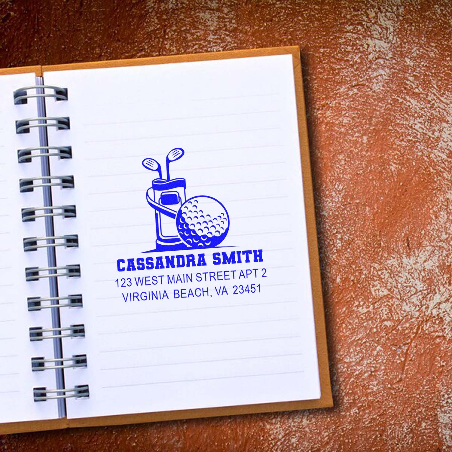 Personalized golf address rubber stamp with name and address, stamped in blue on a notebook page.