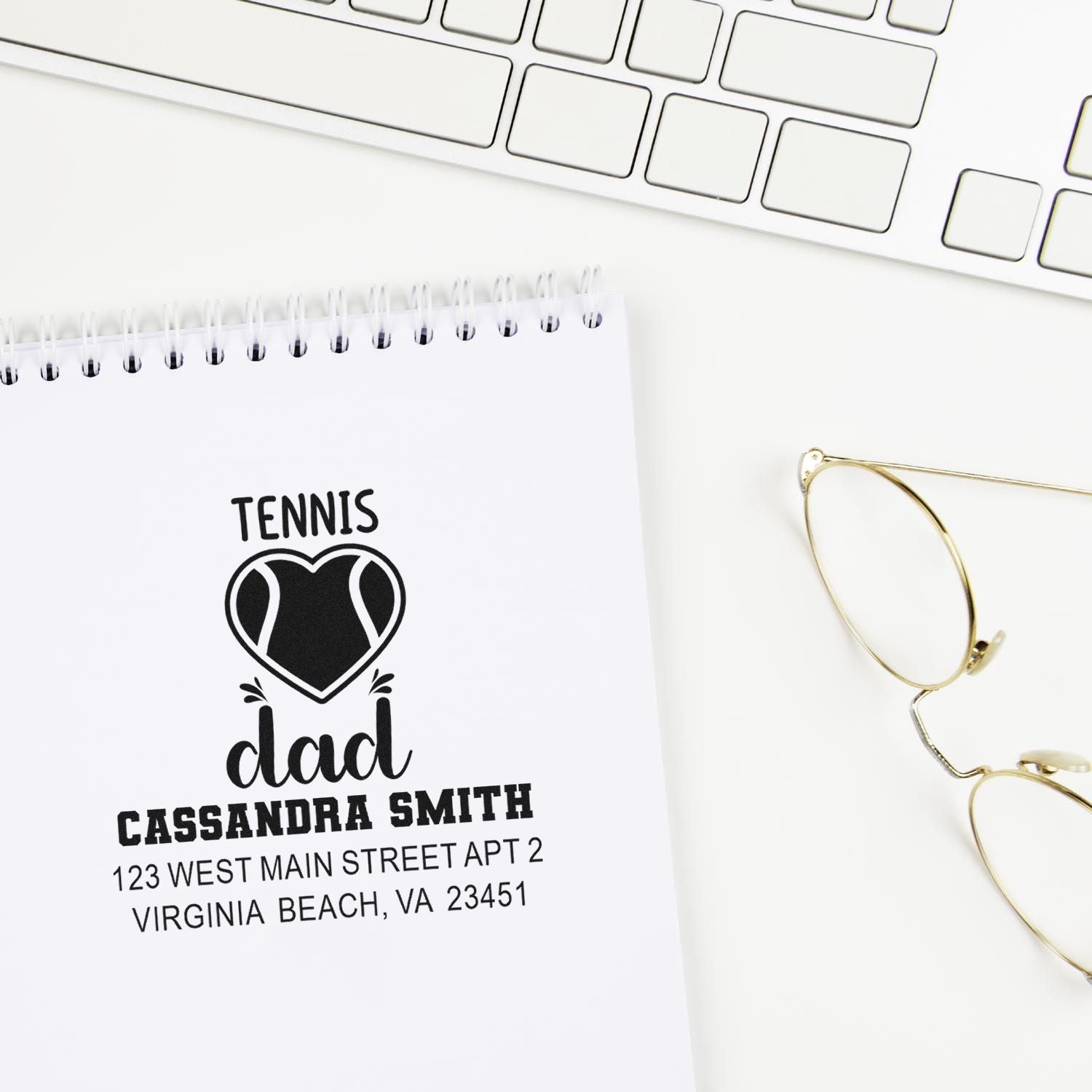 Custom tennis dad rubber stamp with personalized name and return address on notebook, shown on a clean desk with keyboard and glasses.