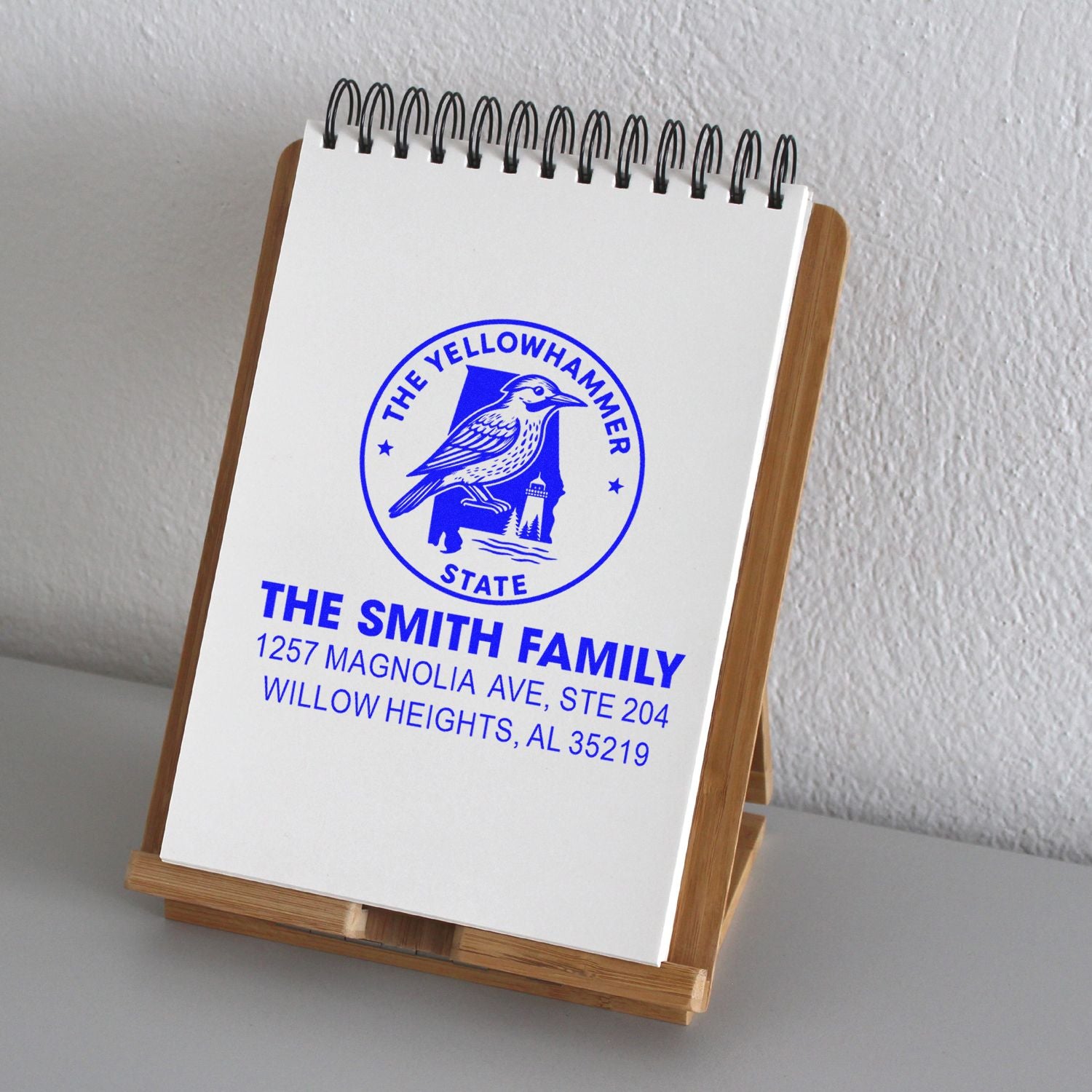 Personalized return address rubber stamp with Yellowhammer State bird logo for The Smith Family, shown on a notebook display stand.