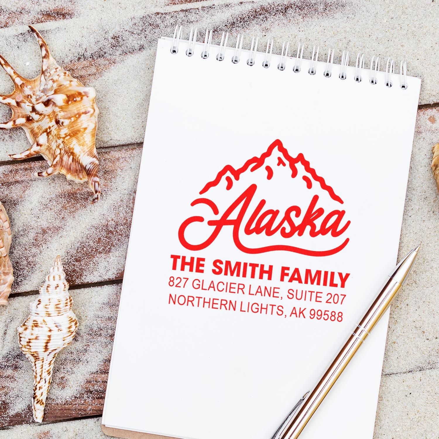 Personalized Alaska return address rubber stamp with family name and address, shown on a notebook for custom mailing use.