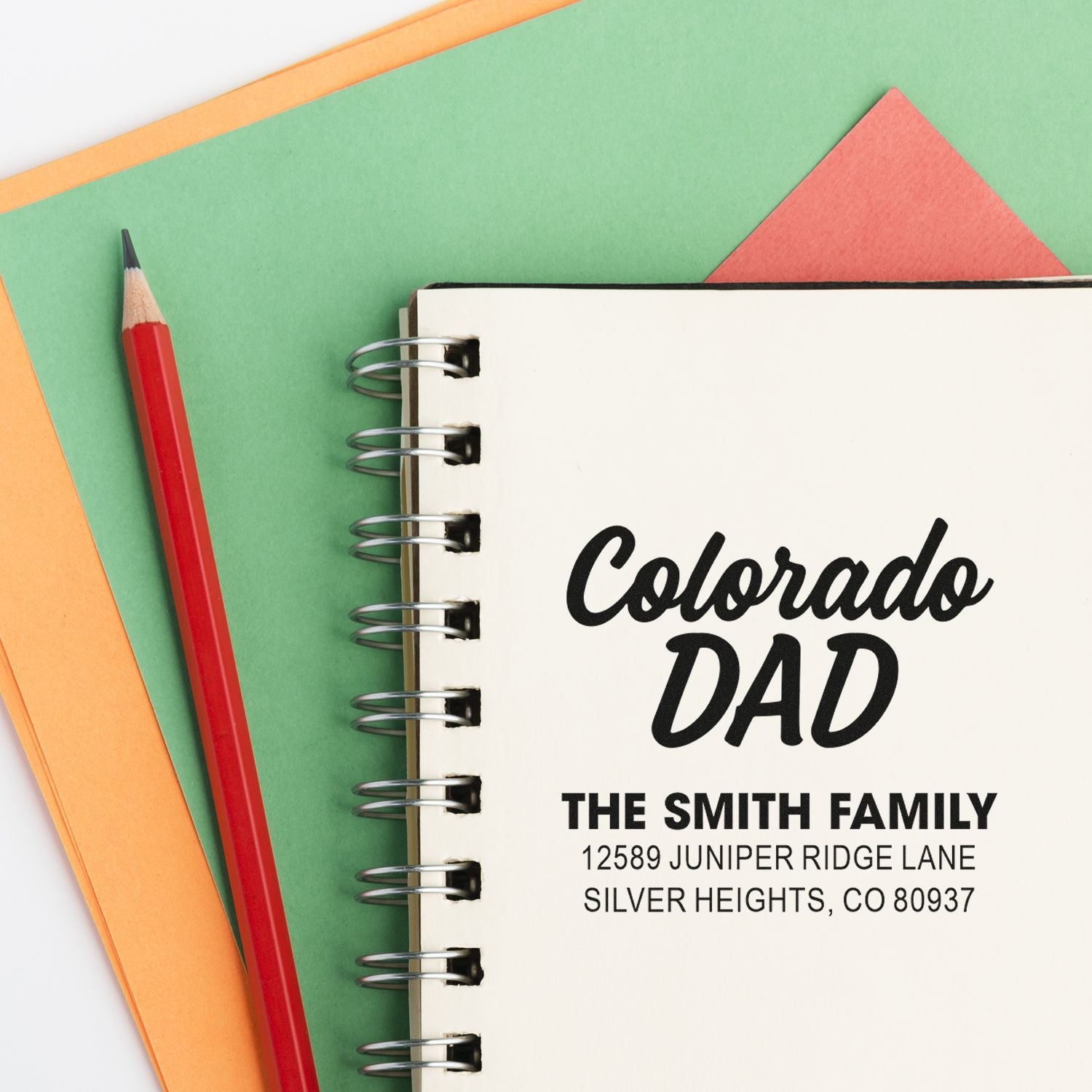 Personalized Colorado Dad rubber stamp design on a notebook with family name and address, shown with pencil and stationery.