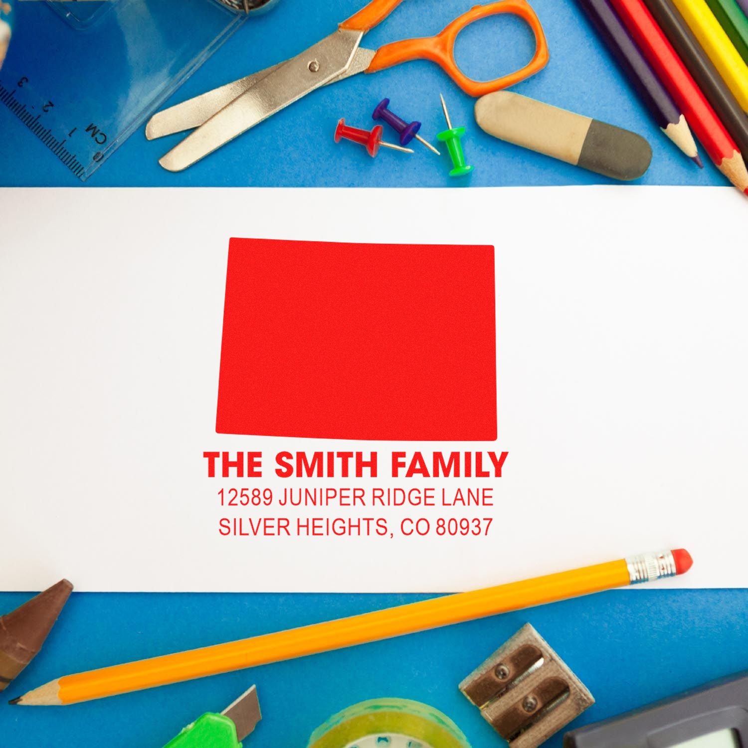Custom return address rubber stamp imprint on envelope with family name and address, styled with colorful school supplies.