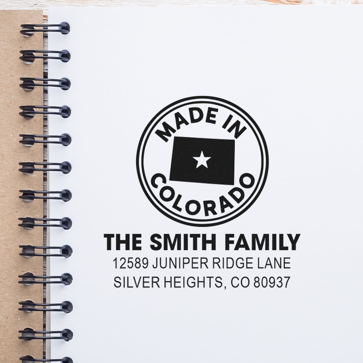 Custom return address rubber stamp for The Smith Family, with Made in Colorado seal, shown on a notebook page.