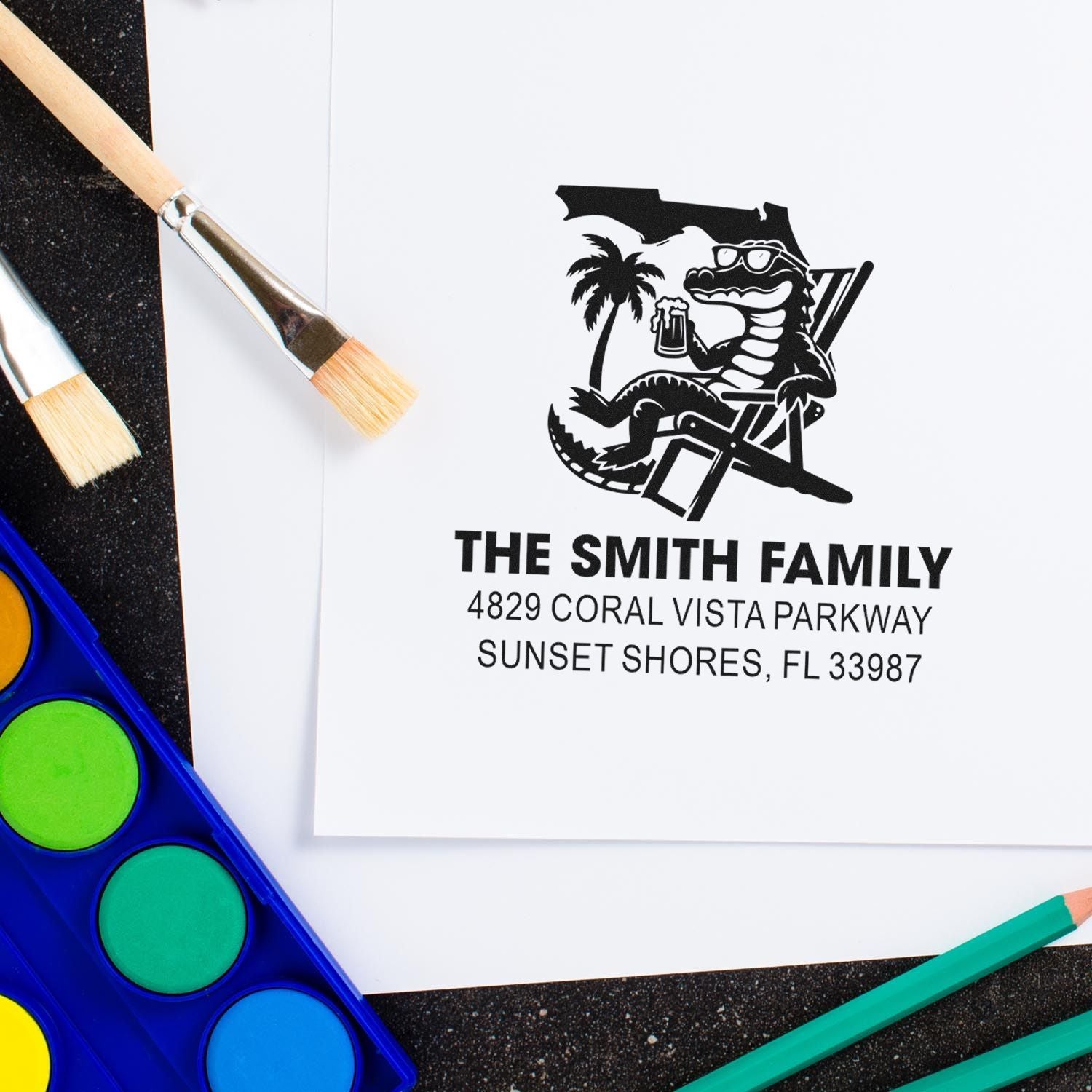 Personalized custom address rubber stamp with Florida alligator design, shown on paper with paintbrushes and watercolor supplies.