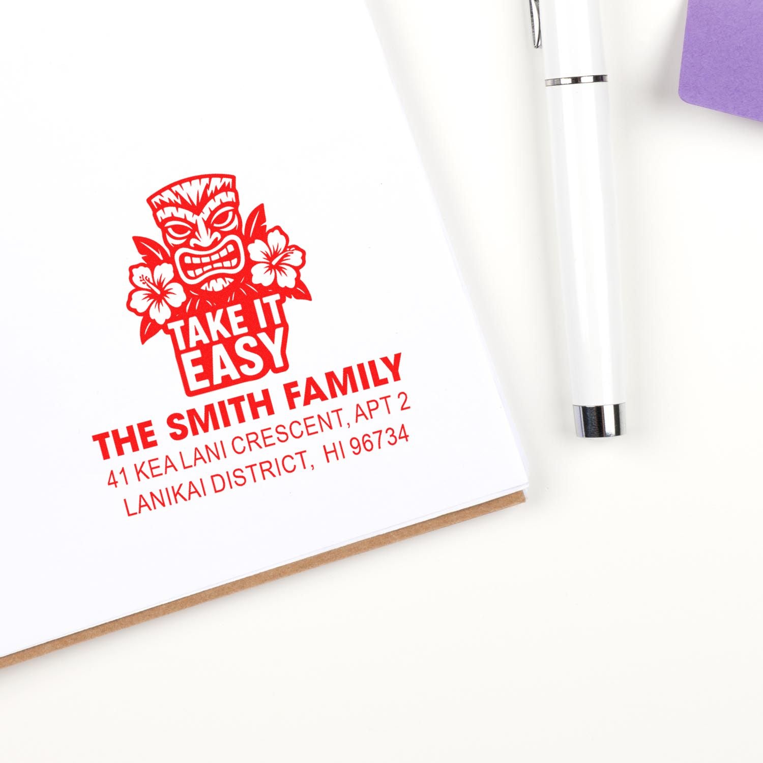 Custom rubber address stamp with tiki Take It Easy design, shown on stationery beside a white pen.