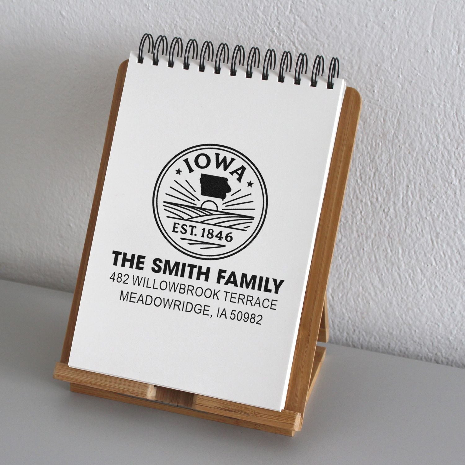 Custom return address rubber stamp with Iowa design, displayed on notepad in a wooden stand.