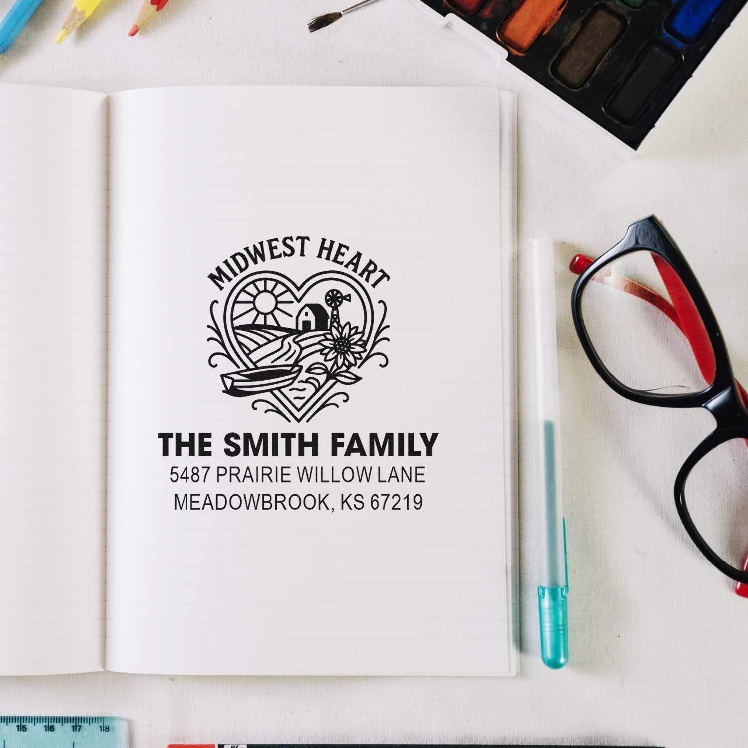 Custom family address rubber stamp with Midwest Heart design, showing name and return address on a notebook mockup.