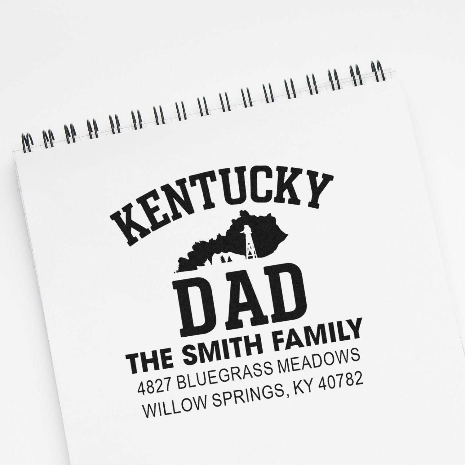 Personalized Kentucky Dad rubber stamp with family name and address, shown on a notebook mockup.