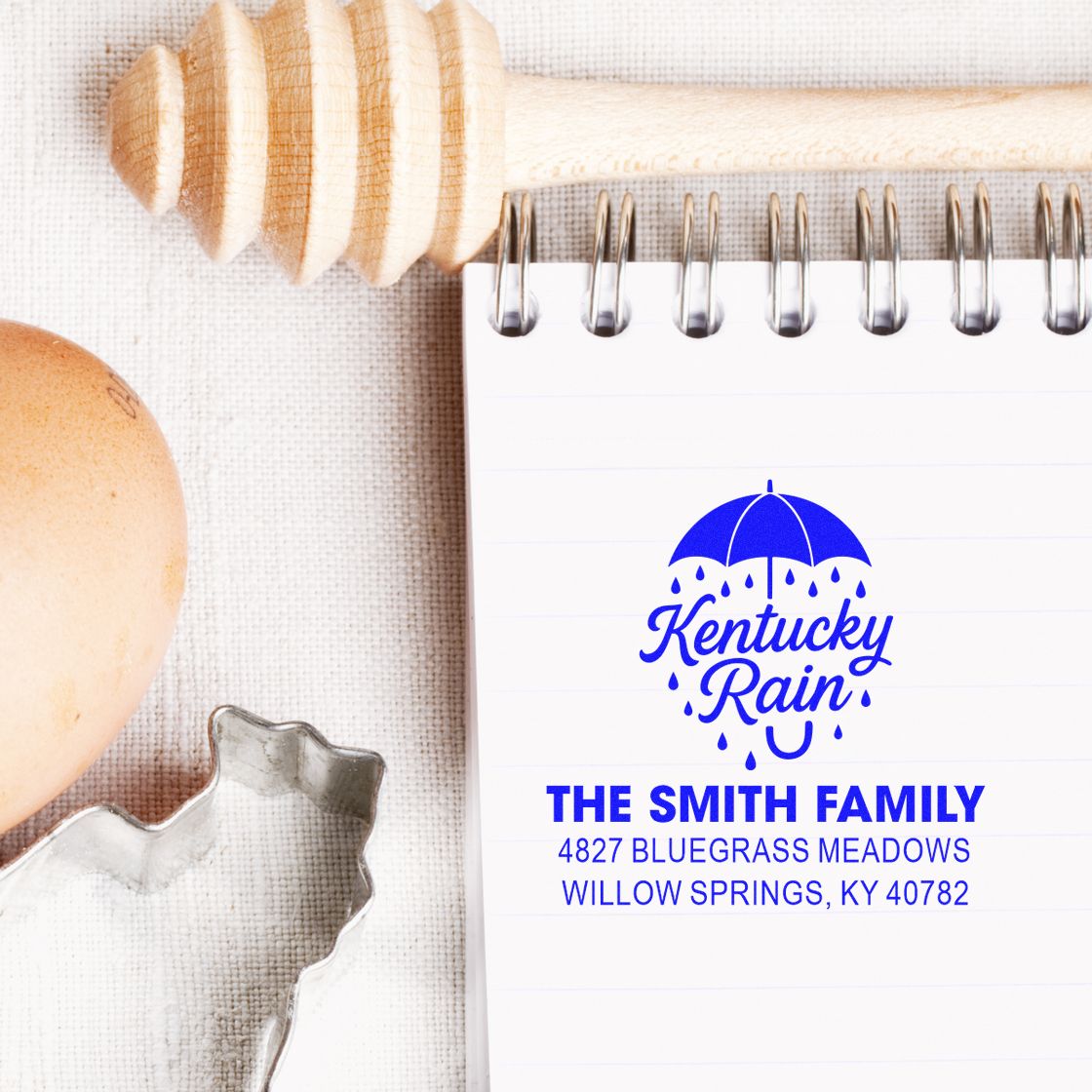Personalized rubber return address stamp with Kentucky Rain umbrella logo and Smith family address on notebook paper.