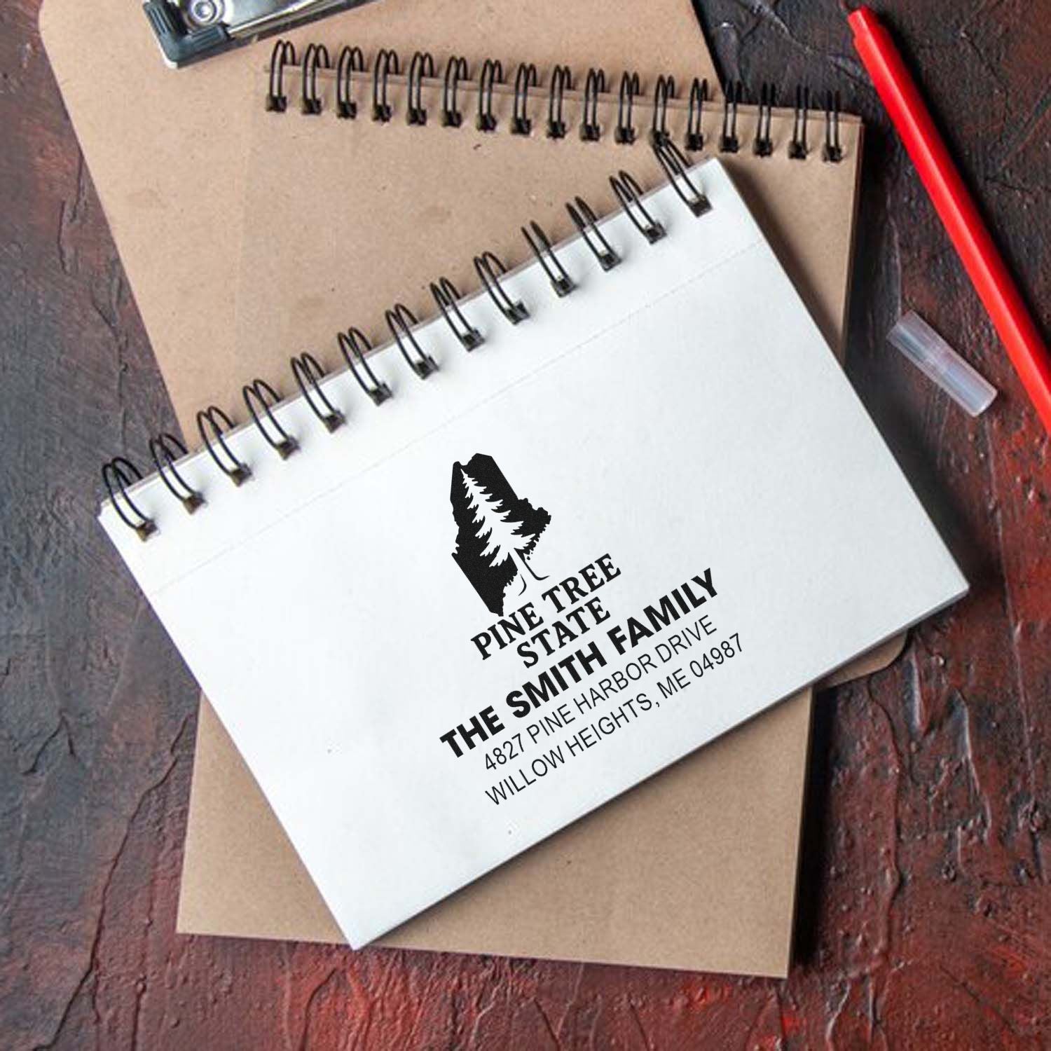 Custom Pine Tree State family return address rubber stamp shown on a notebook for personalized mailing and crafts.