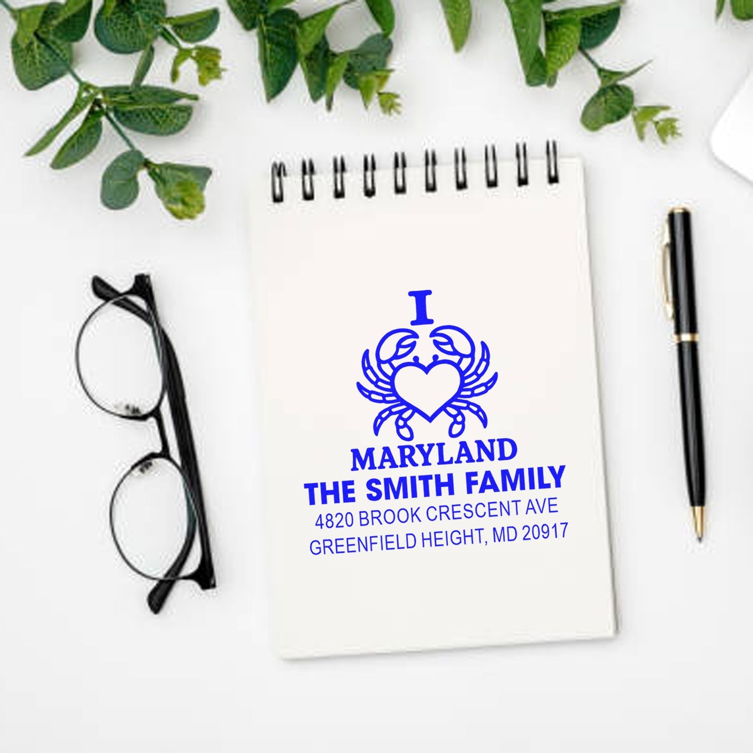 Custom Maryland rubber stamp with crab heart logo and family address, shown on notebook stationery mockup.