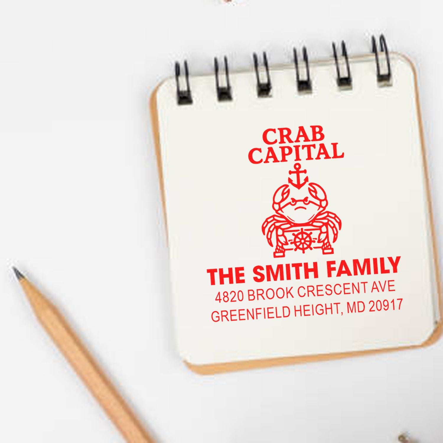 Personalized return address rubber stamp with Crab Capital crab design, custom family name and address on notebook.