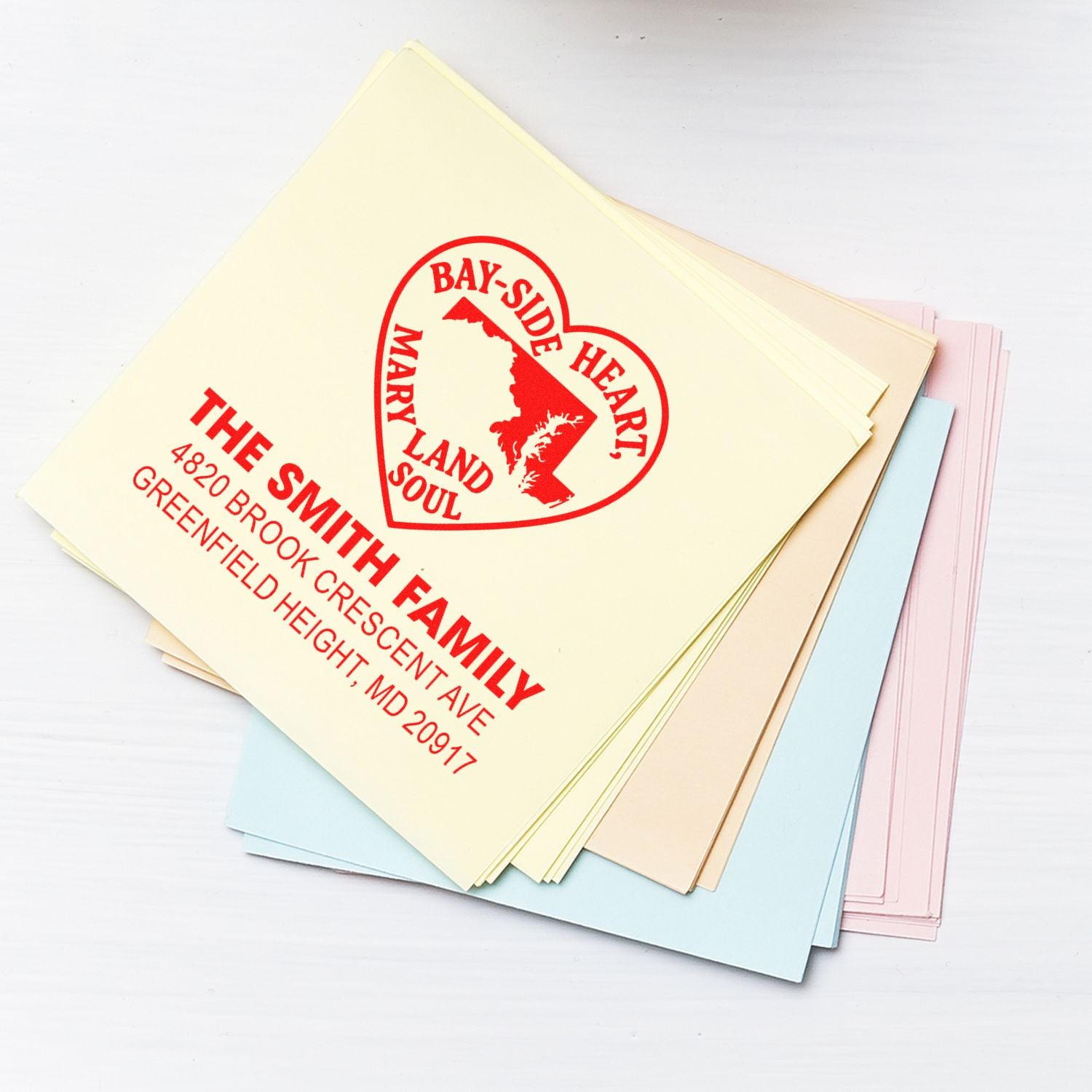 Custom rubber address stamp imprint on pastel paper stack, featuring The Smith Family Bay Side Heart return address design.