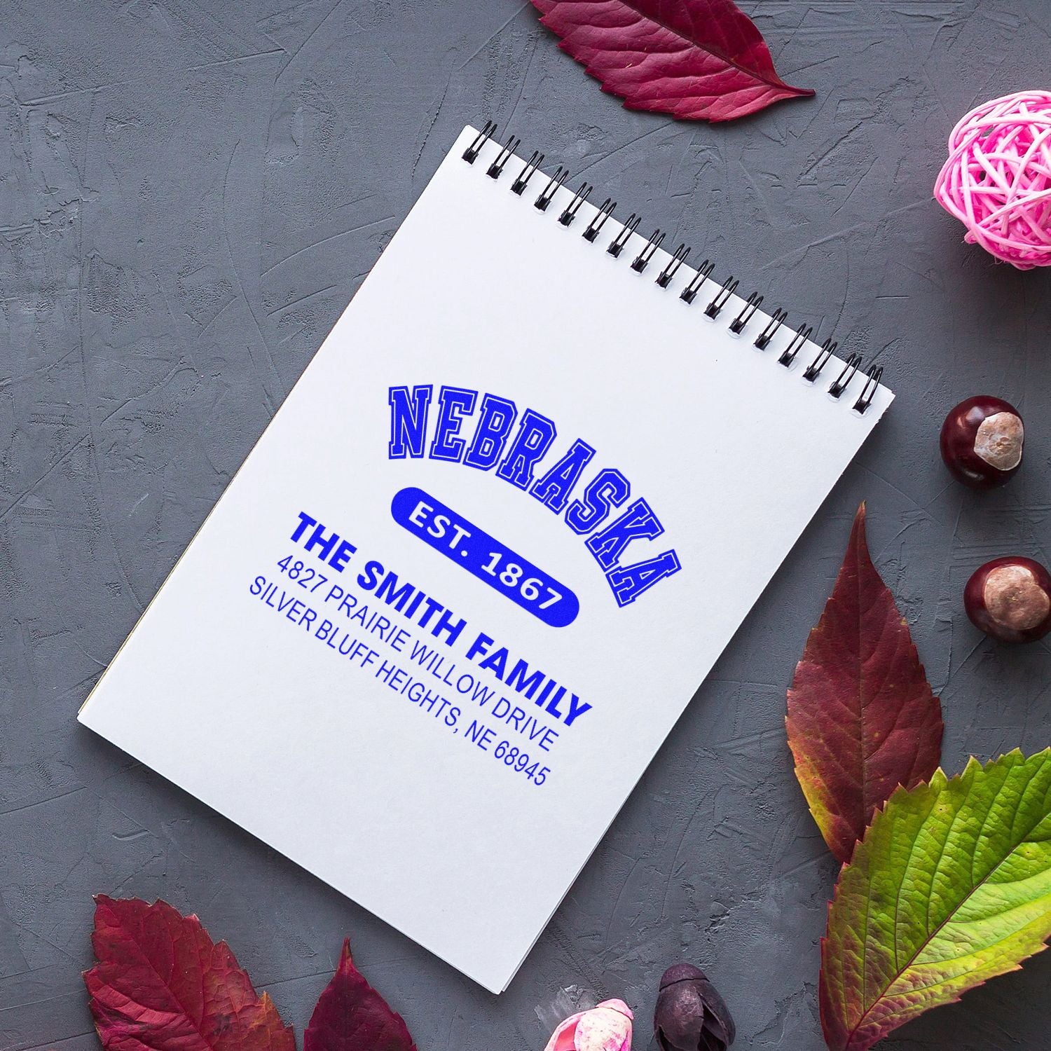 Custom return address rubber stamp in blue ink featuring Nebraska and The Smith Family, shown on a spiral notebook.