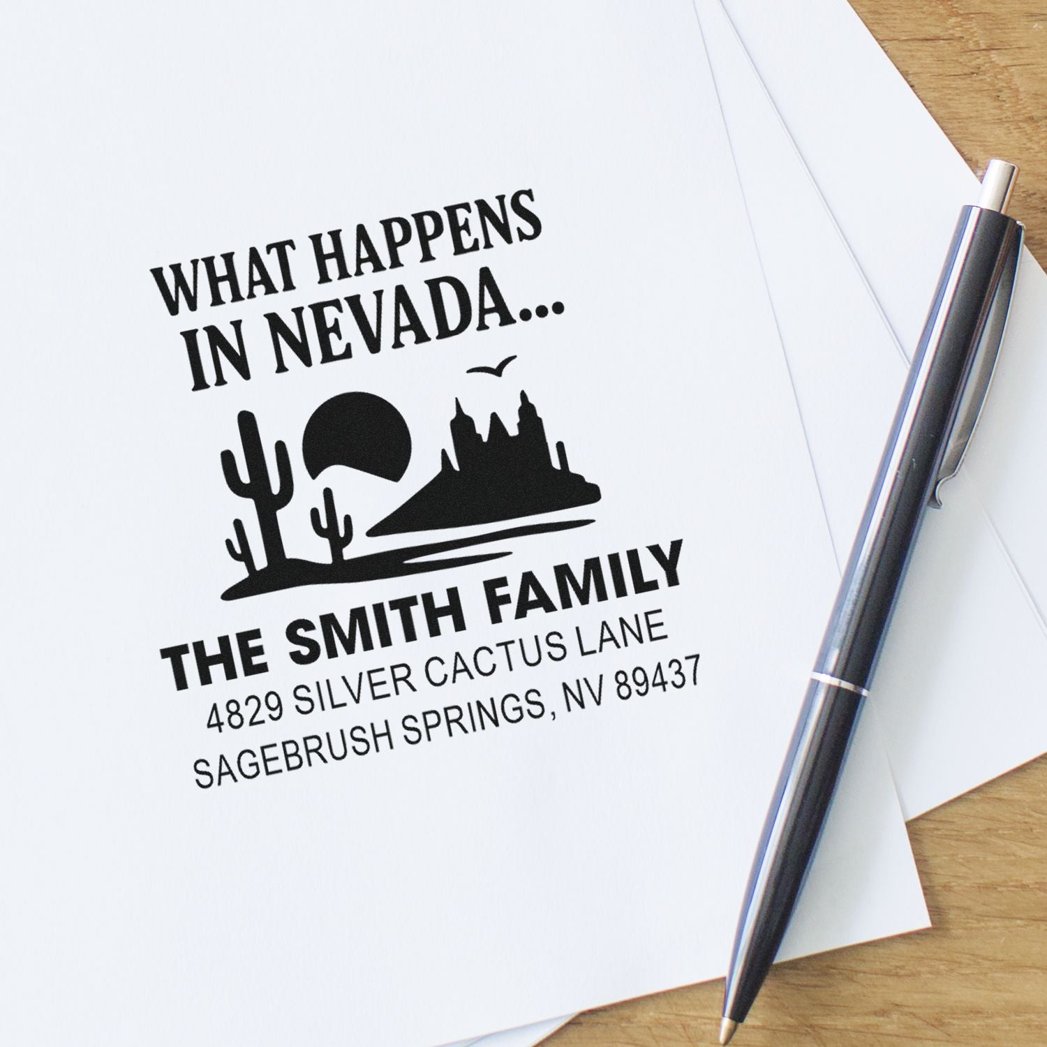 Custom rubber return address stamp for The Smith Family, Nevada, with desert graphic on paper beside pen.