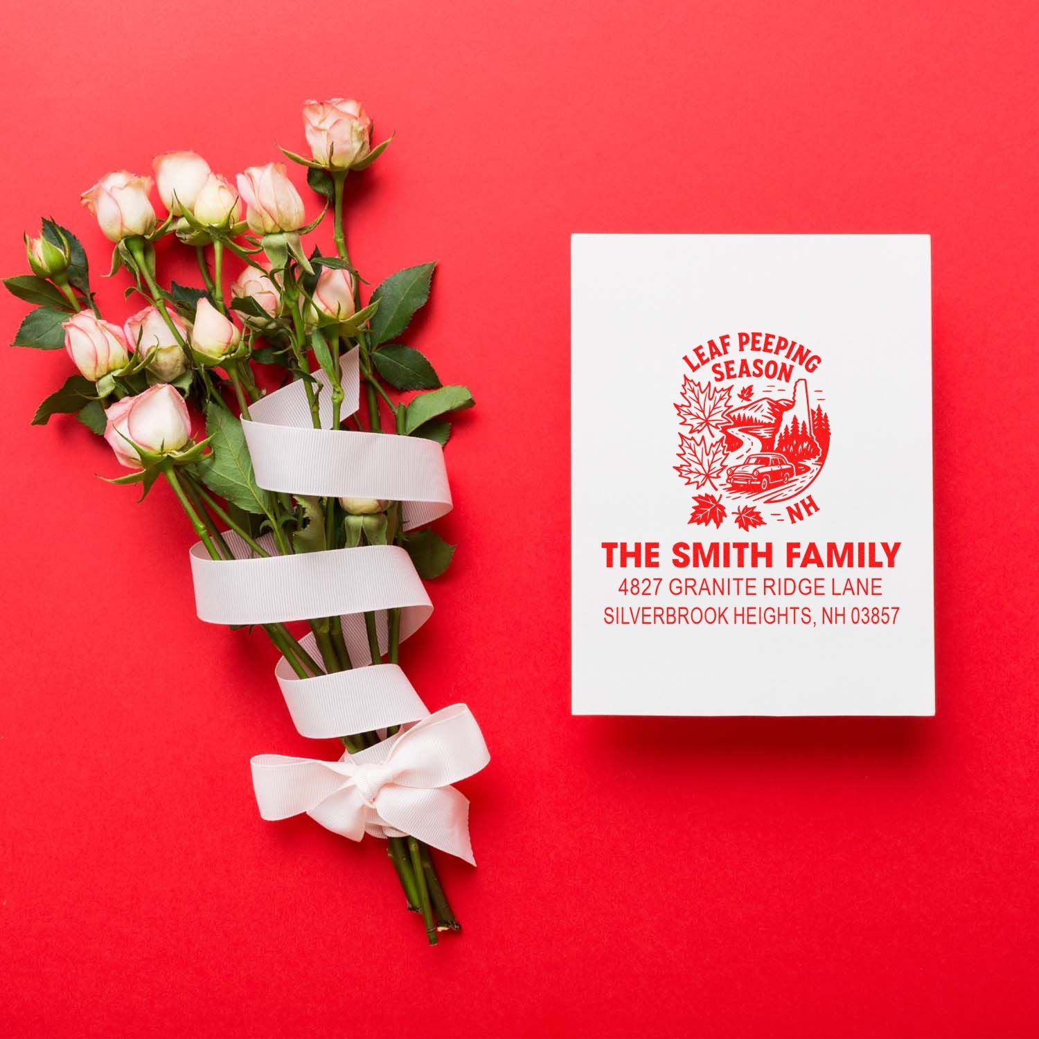 Personalized return address rubber stamp with “Leaf Peeping Season” design beside wrapped roses on a red background