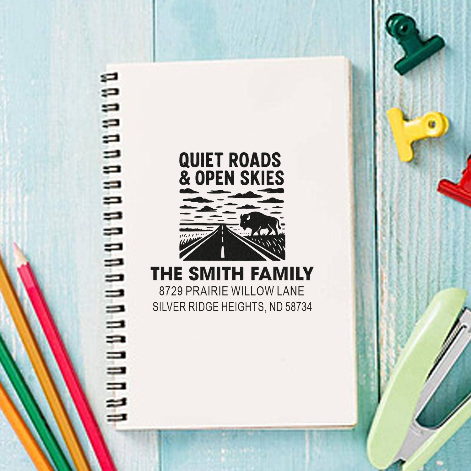 Custom family return address rubber stamp with road and bison design on a notebook.