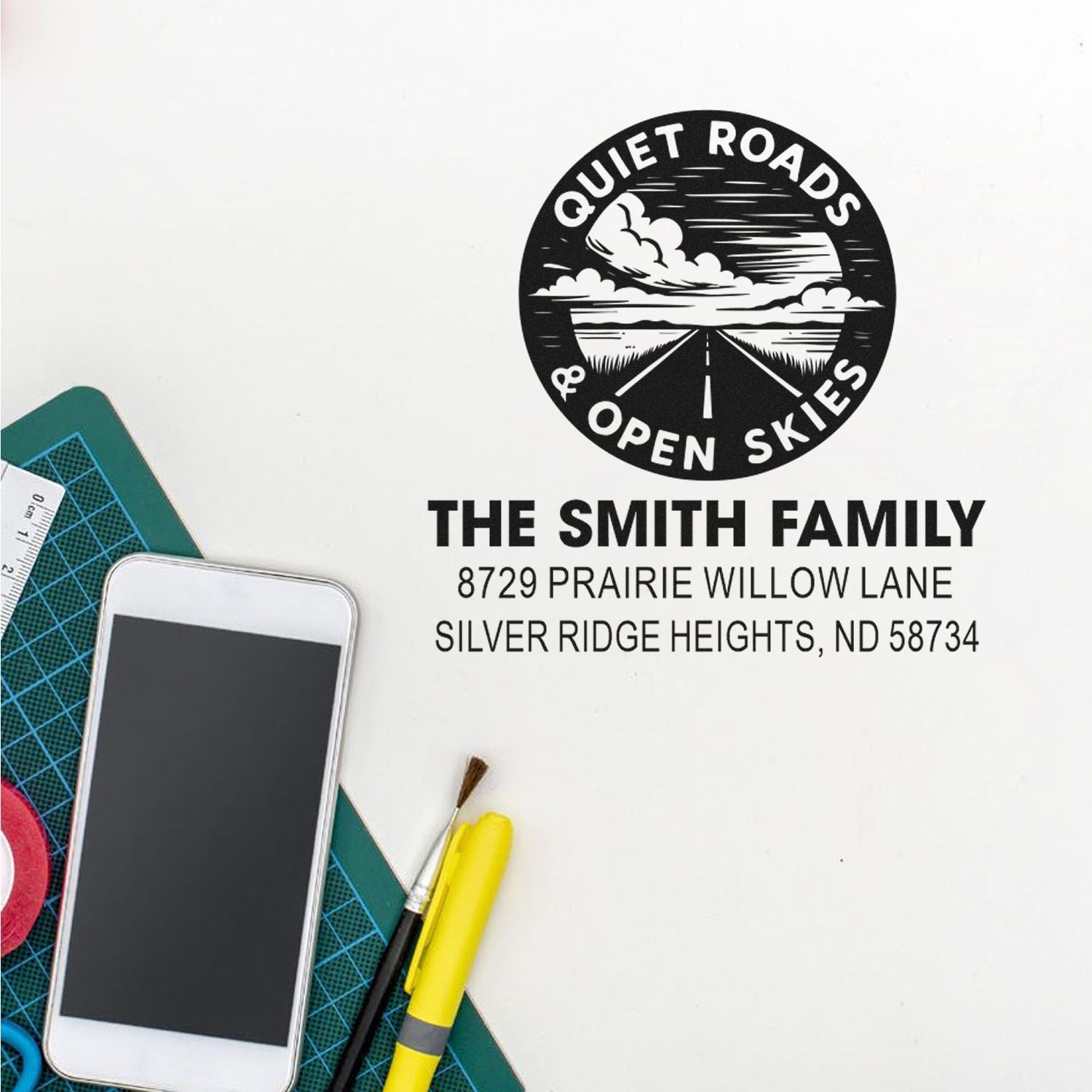 Custom address rubber stamp with family name and scenic Quiet Roads & Open Skies logo for personalized mailing and craft projects.