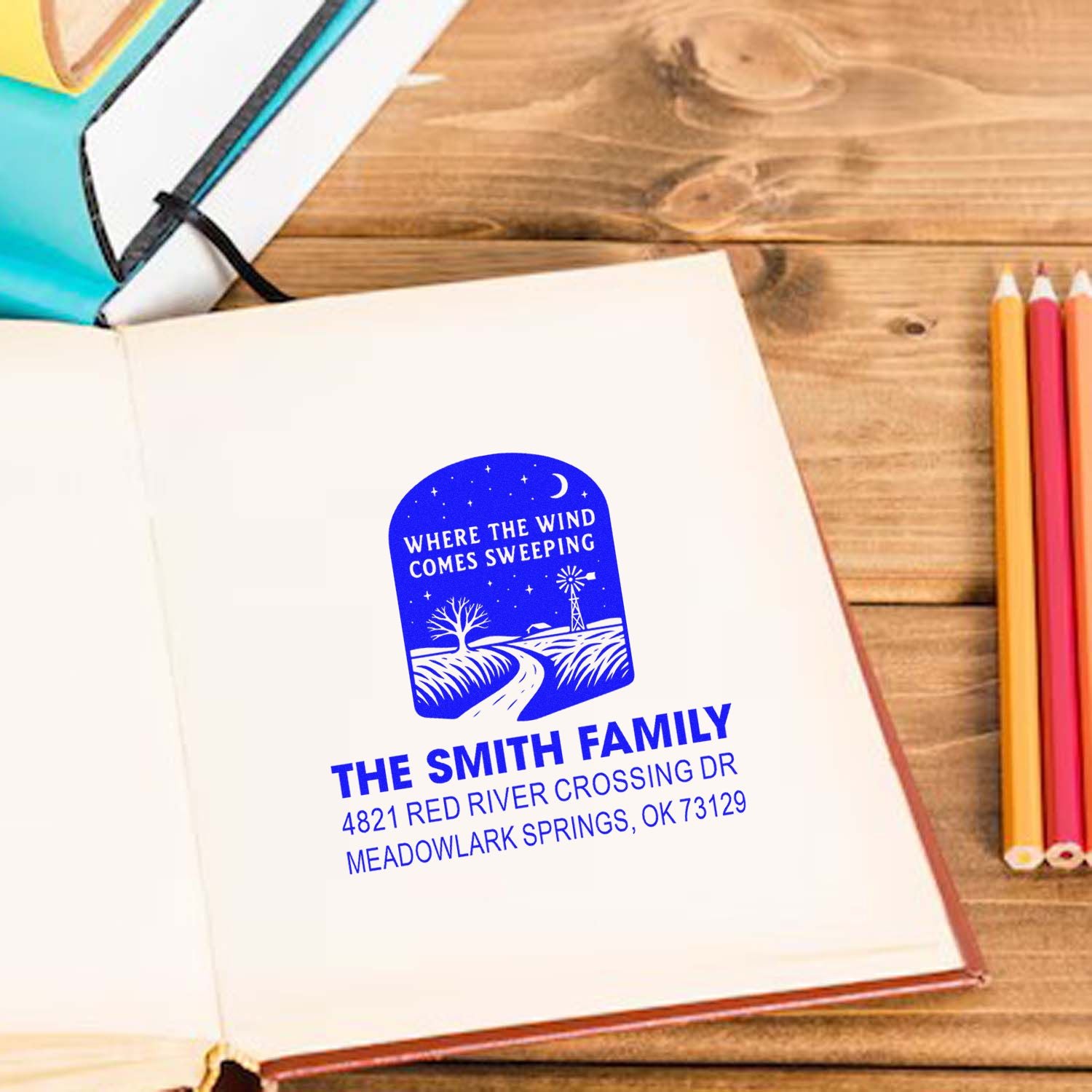 Custom family return address rubber stamp with windmill design, showing blue ink imprint on notebook for personalized stationery.