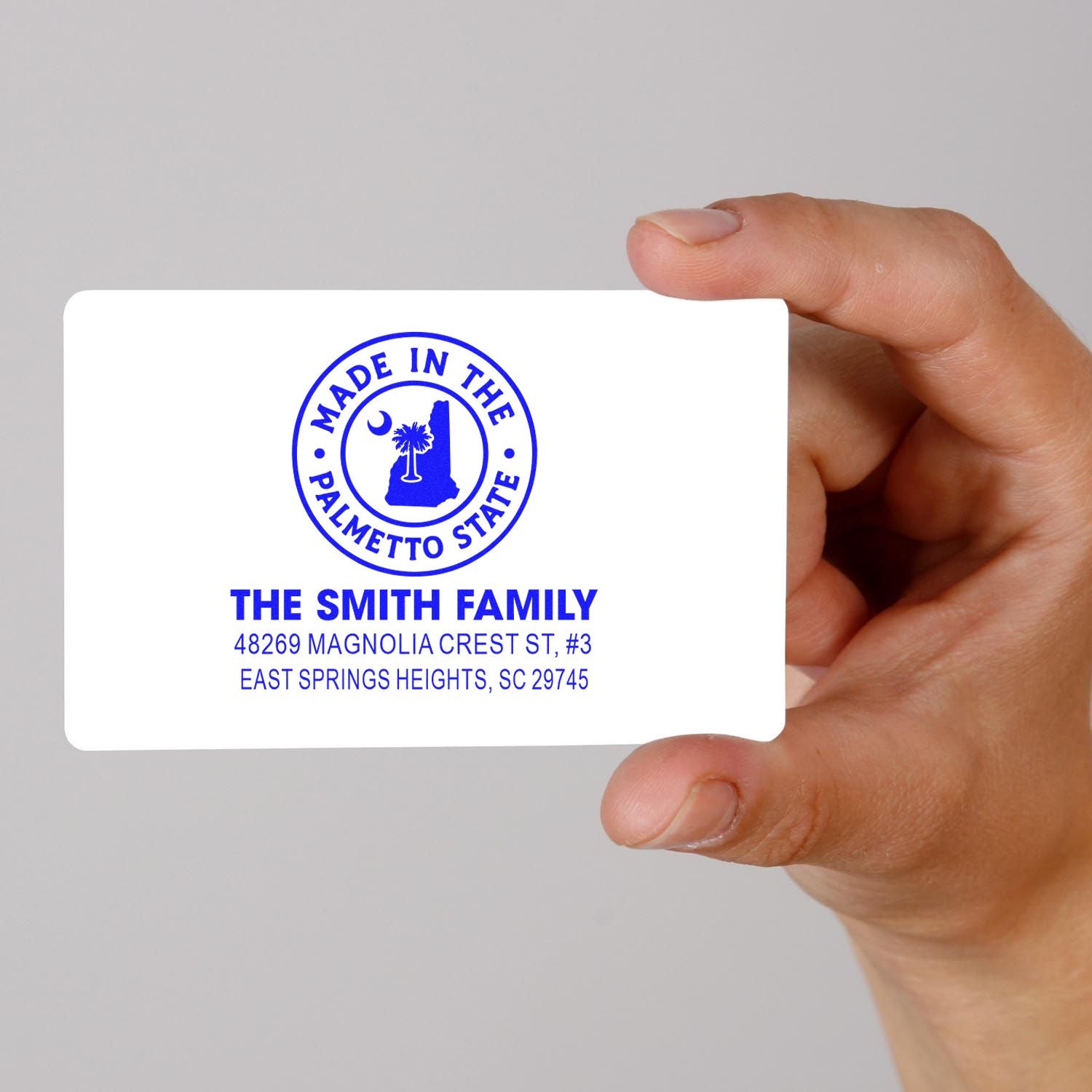 Hand holding custom rubber stamp sample with family name, address, and South Carolina Made in the Palmetto State logo.