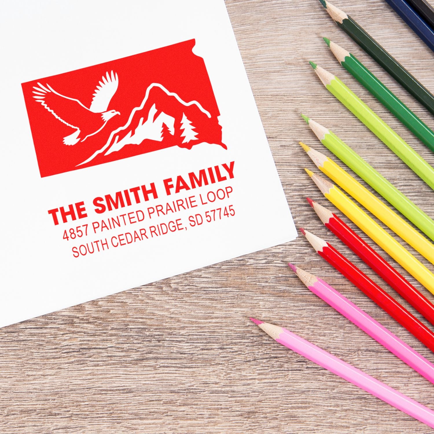 Custom family address rubber stamp with eagle and mountain logo, displayed with colored pencils for personalized stationery.