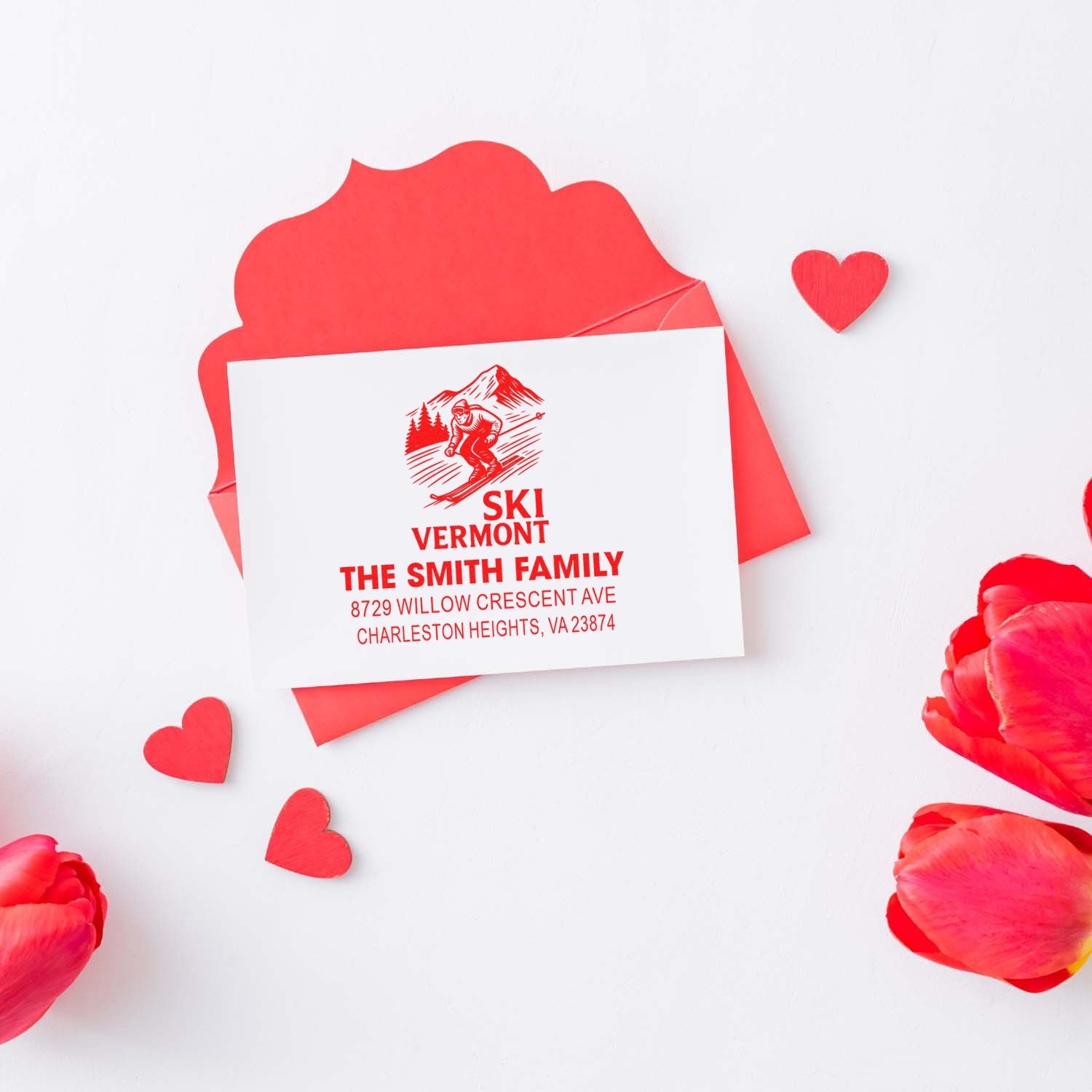 Custom red ski Vermont return address stamp on white card with red envelope, heart accents, and flower petals for a romantic stationery display.