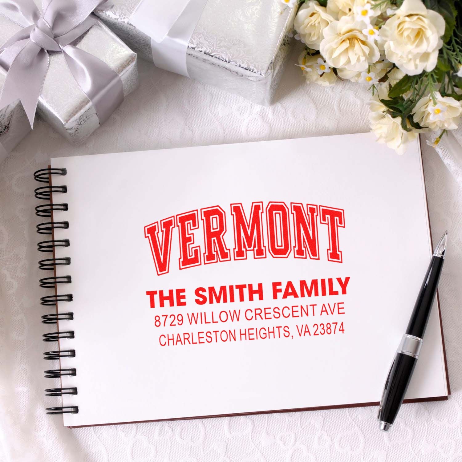 Personalized Vermont address stamp for The Smith Family, shown on a spiral notebook with ribbon-wrapped gifts, flowers, and pen.