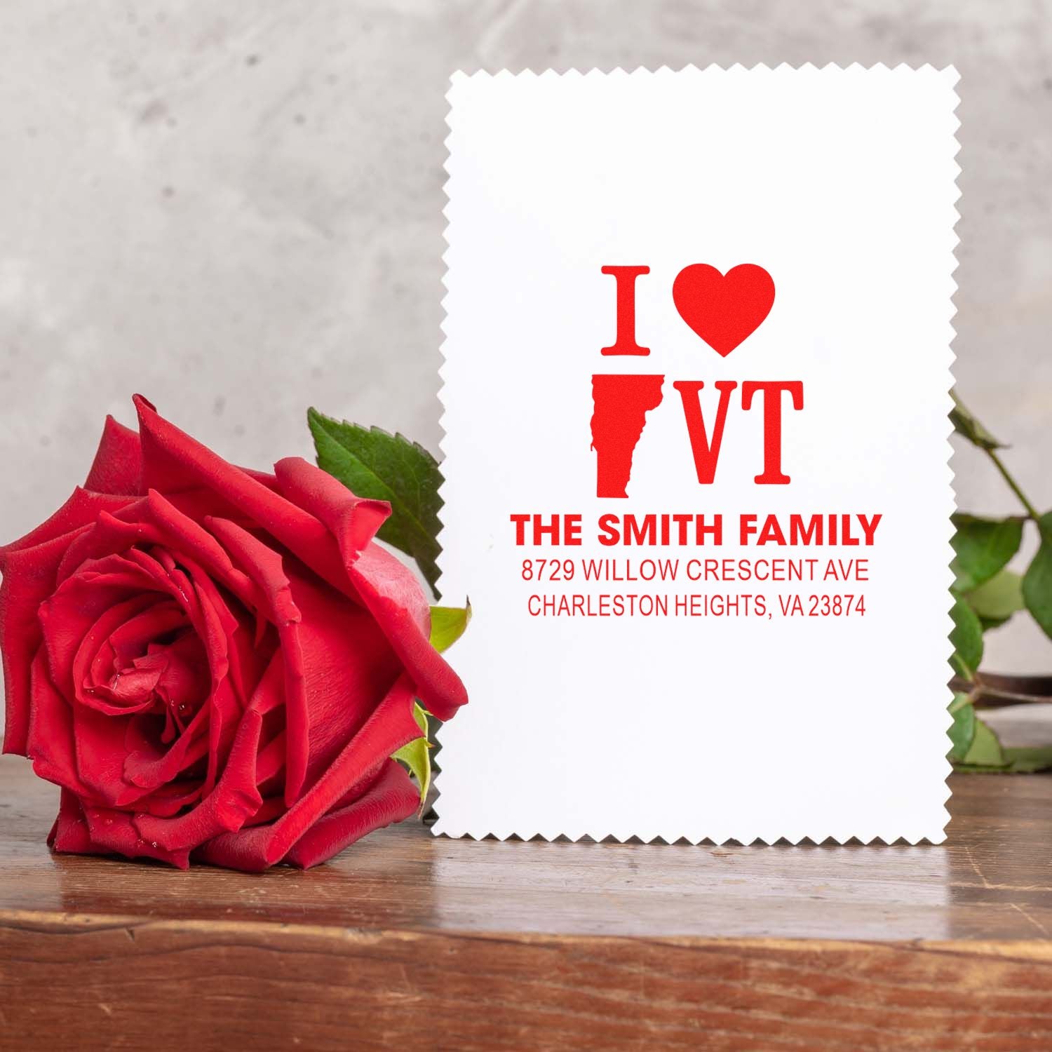 Personalized I Heart VT address stamp with family name and address beside a red rose on a wooden table.