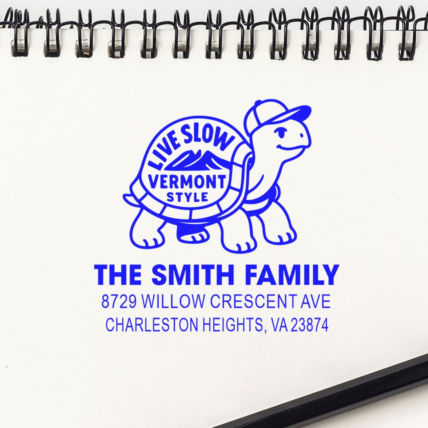 Blue custom address stamp on a spiral notebook page, featuring a turtle logo and Live Slow Vermont Style for The Smith Family, Charleston Heights, VA.