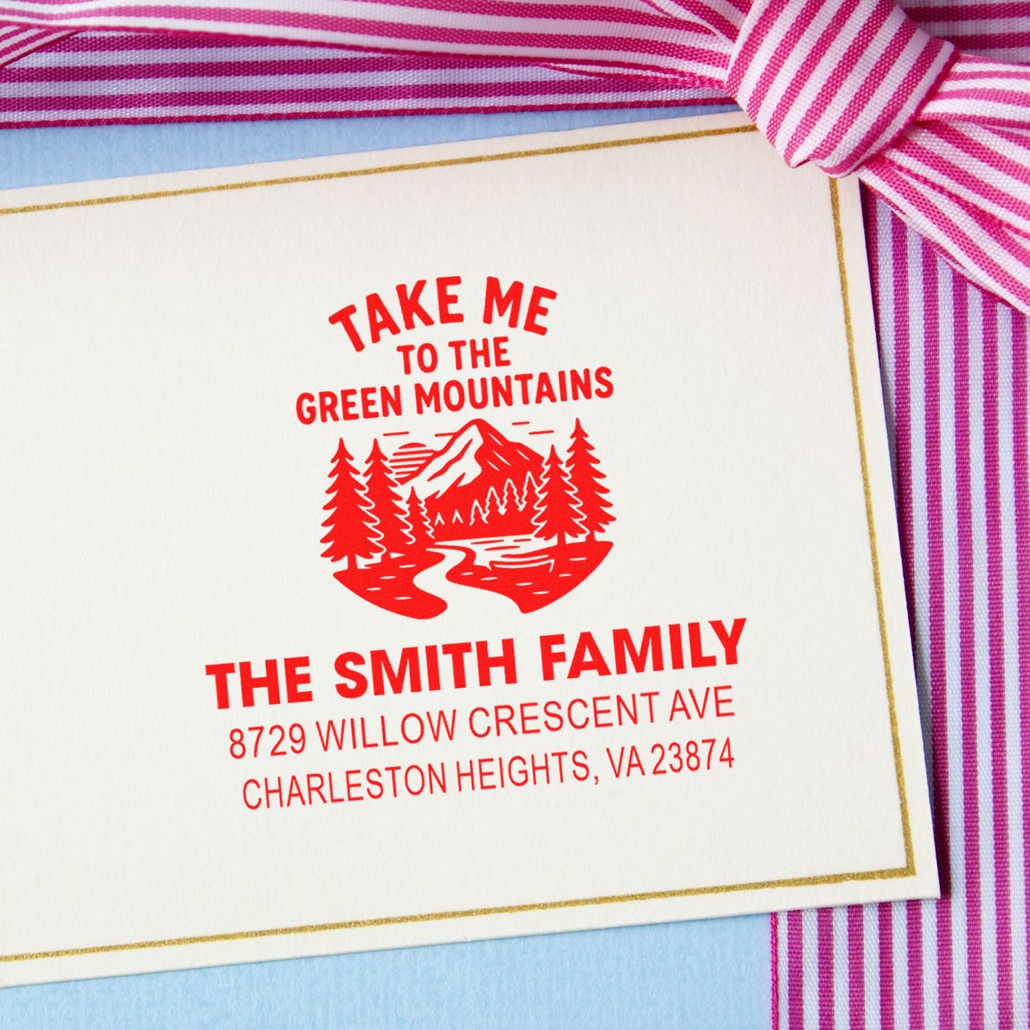 Custom family return address stamp with red Green Mountains graphic on white stationery, framed by pink striped ribbon and gold border.