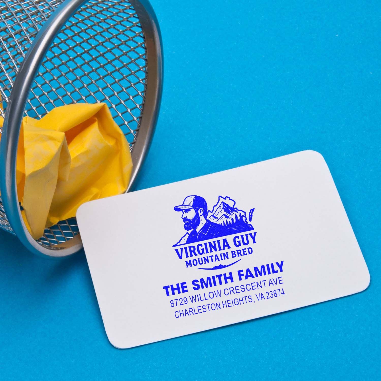 Personalized return address stamp with Virginia Guy mountain logo beside a mesh desk pen cup on a blue background, featuring The Smith Family address.