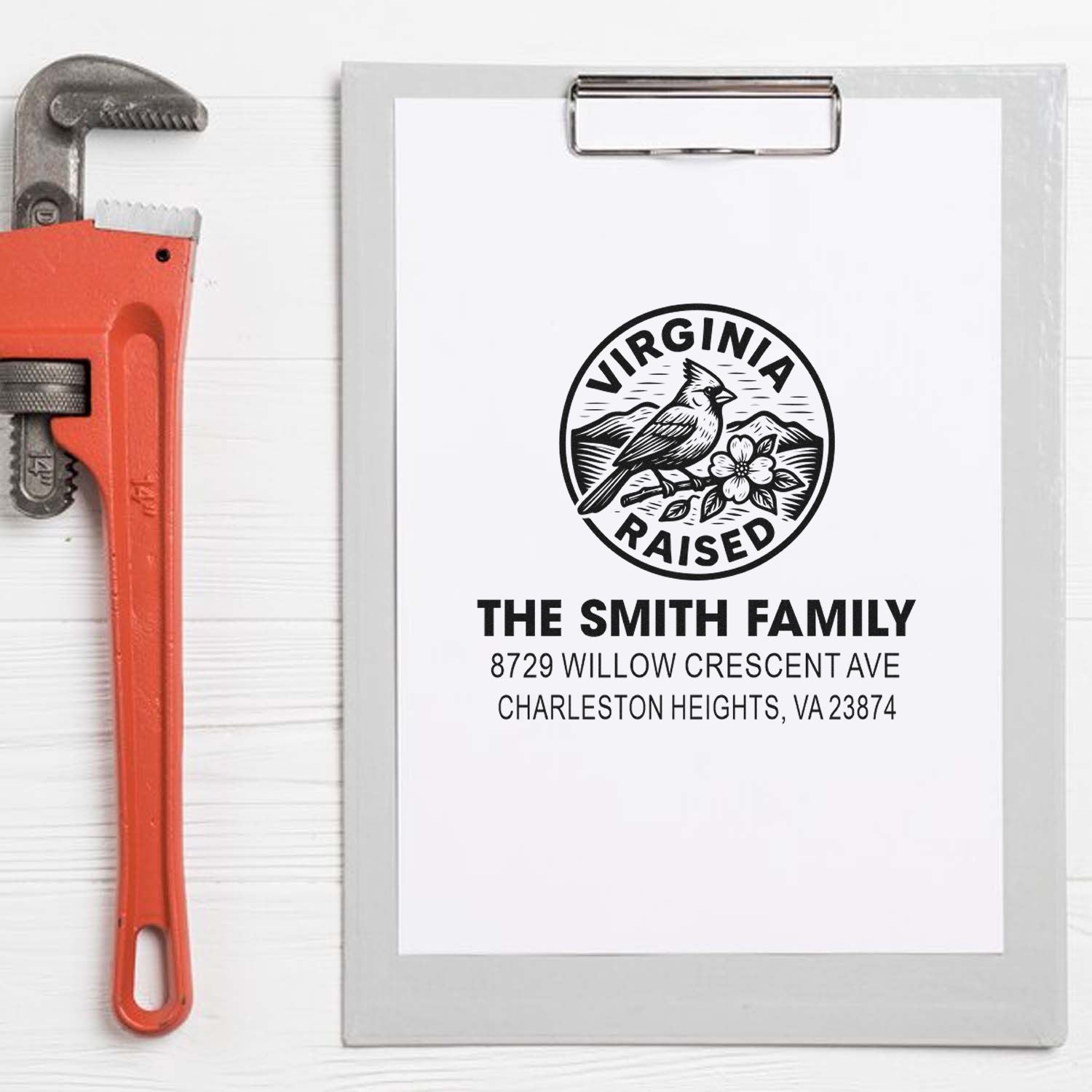 Personalized Virginia Raised family address stamp on clipboard beside pipe wrench, featuring cardinals, mountains, and The Smith Family address.