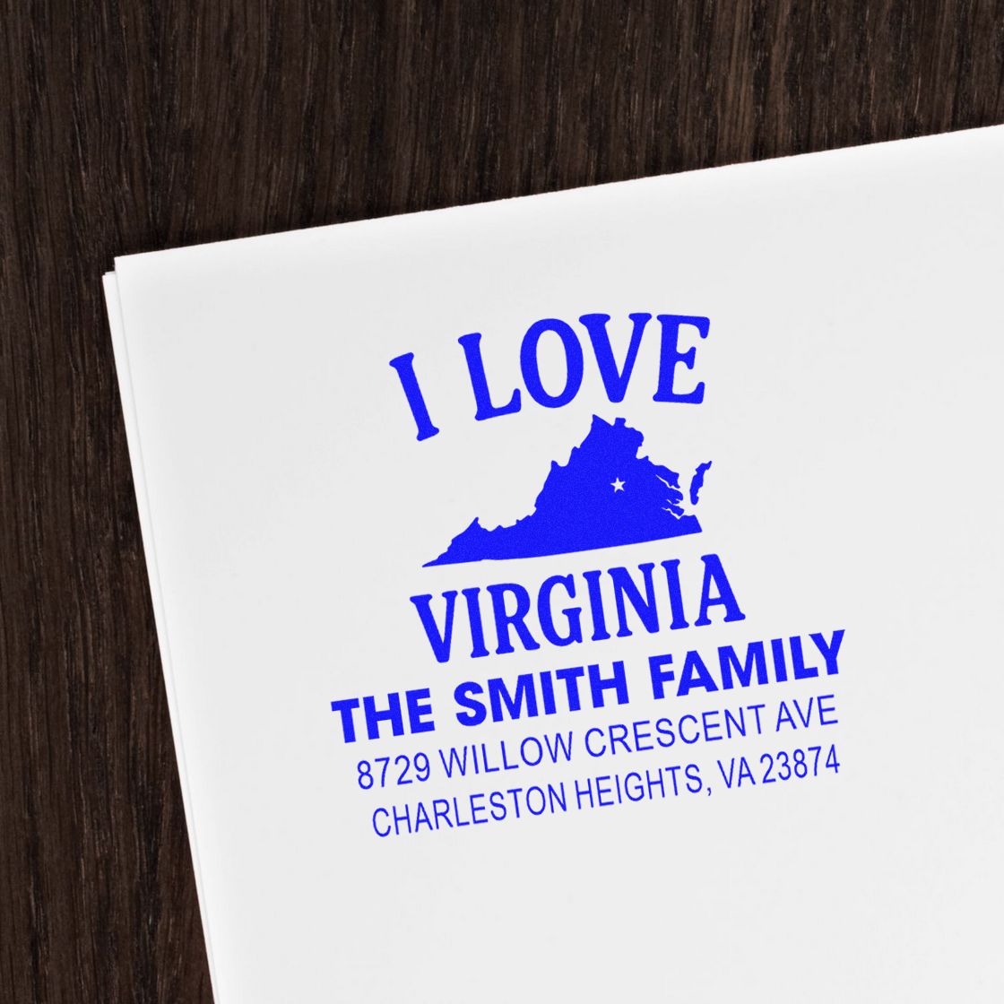 Custom blue Virginia address stamp on white paper, reading I Love Virginia with The Smith Family name and Charleston Heights address on a dark wood table.