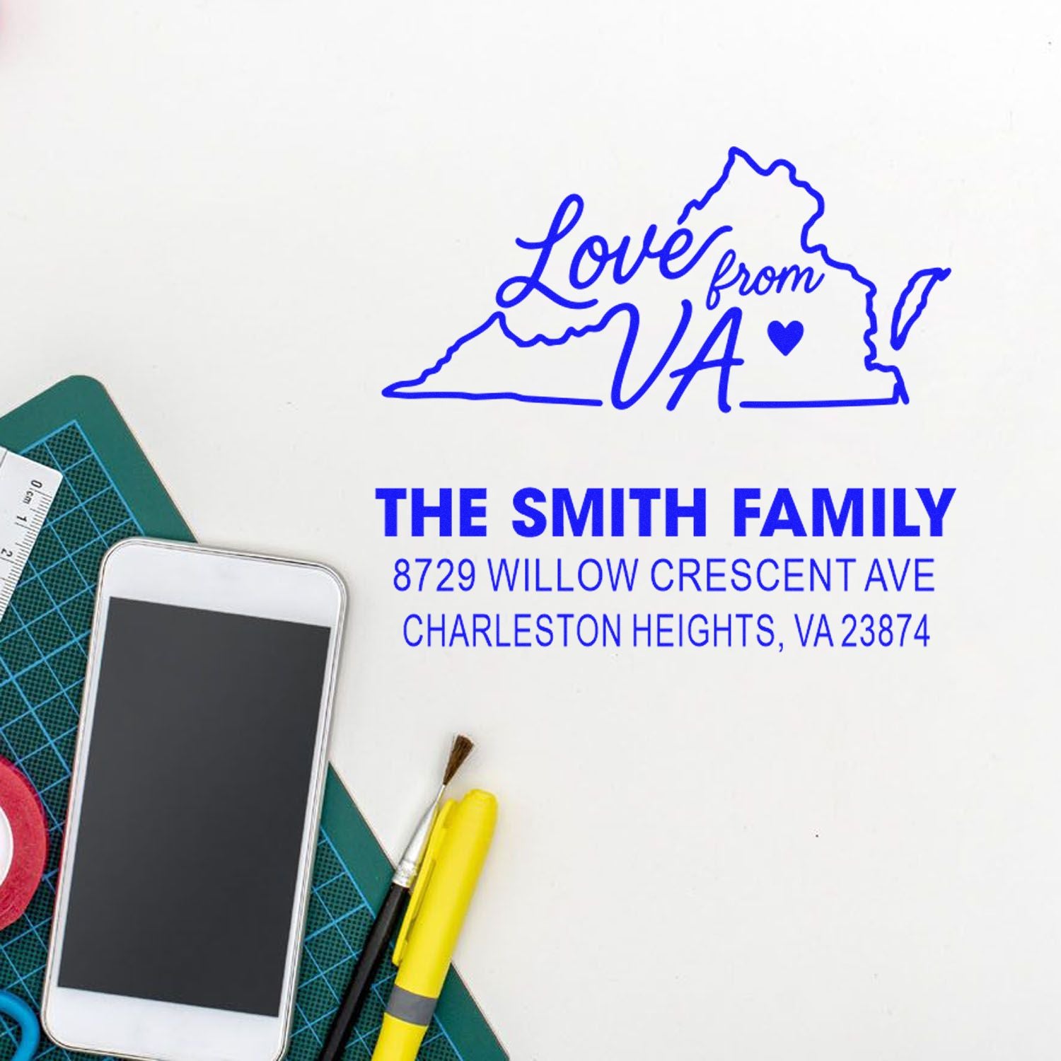 Custom Virginia return address stamp with Love from VA state outline, family name, and address on a craft workspace with phone, ruler, and cutting mat.