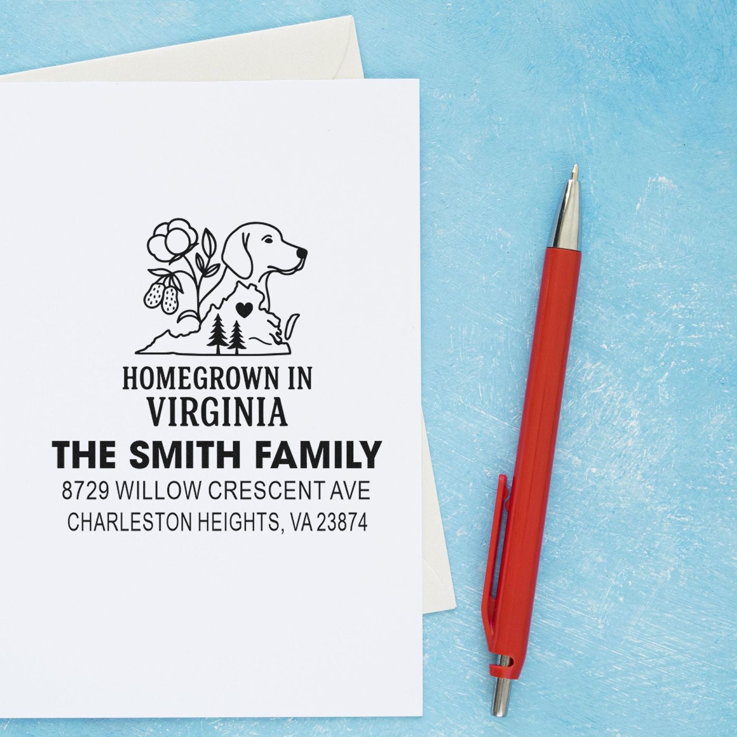 Custom Homegrown in Virginia family address stamp on white paper, with dog and floral design, beside a red pen on a blue textured background.