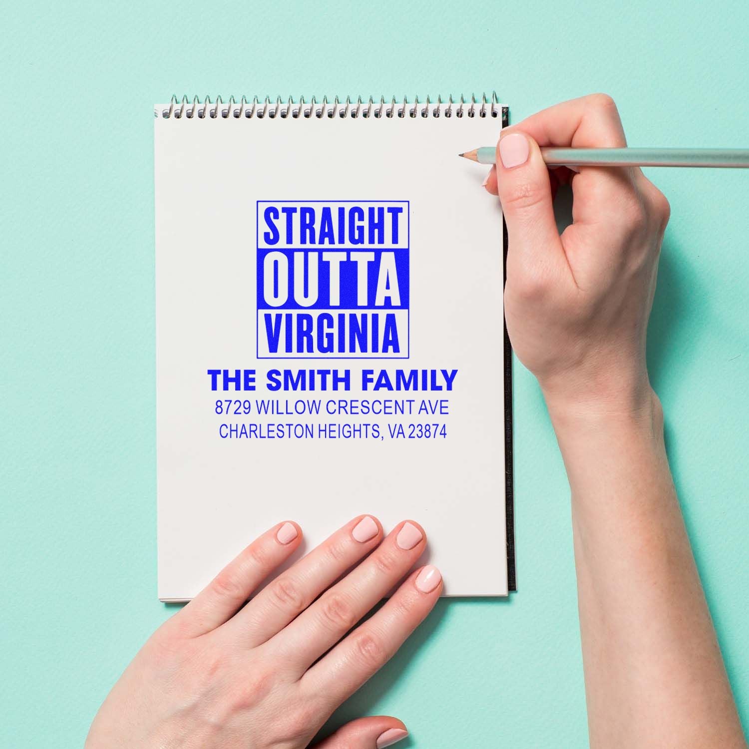 Custom address stamp on a spiral notebook, reading Straight Outta Virginia with The Smith Family address, held by hands on a mint background.