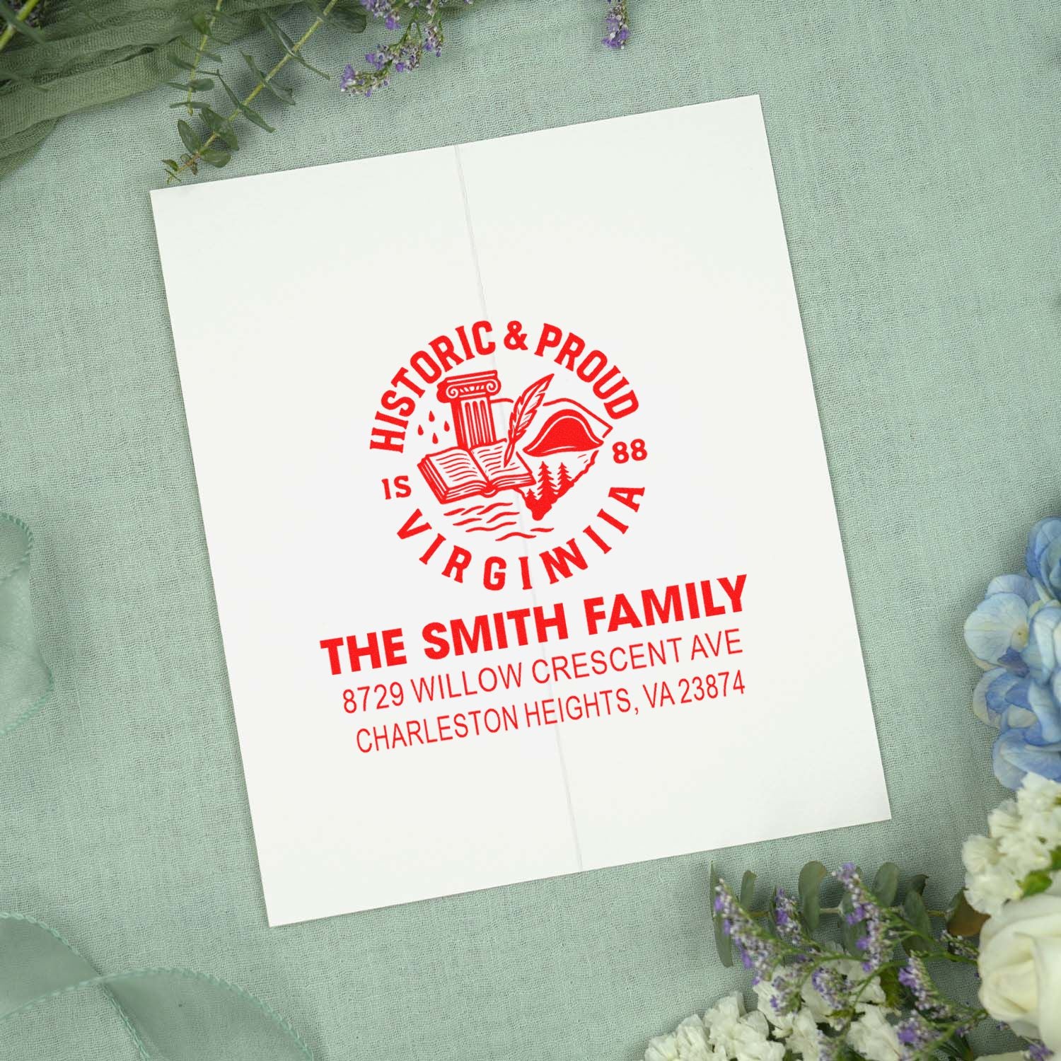Custom red self-inking stamp on folded card, reading Historic & Proud Virginia for The Smith Family, styled on pastel fabric with flowers.
